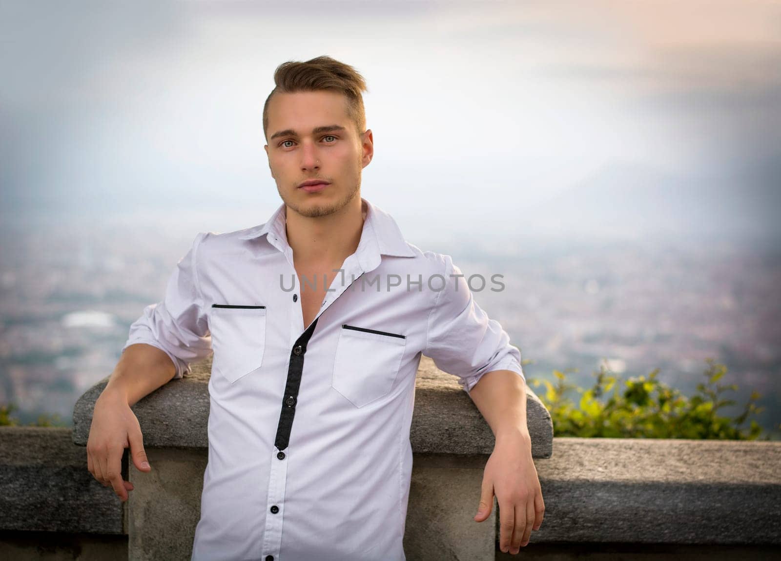 Blond young man on top of hill above Turin, Italy, with city behind him