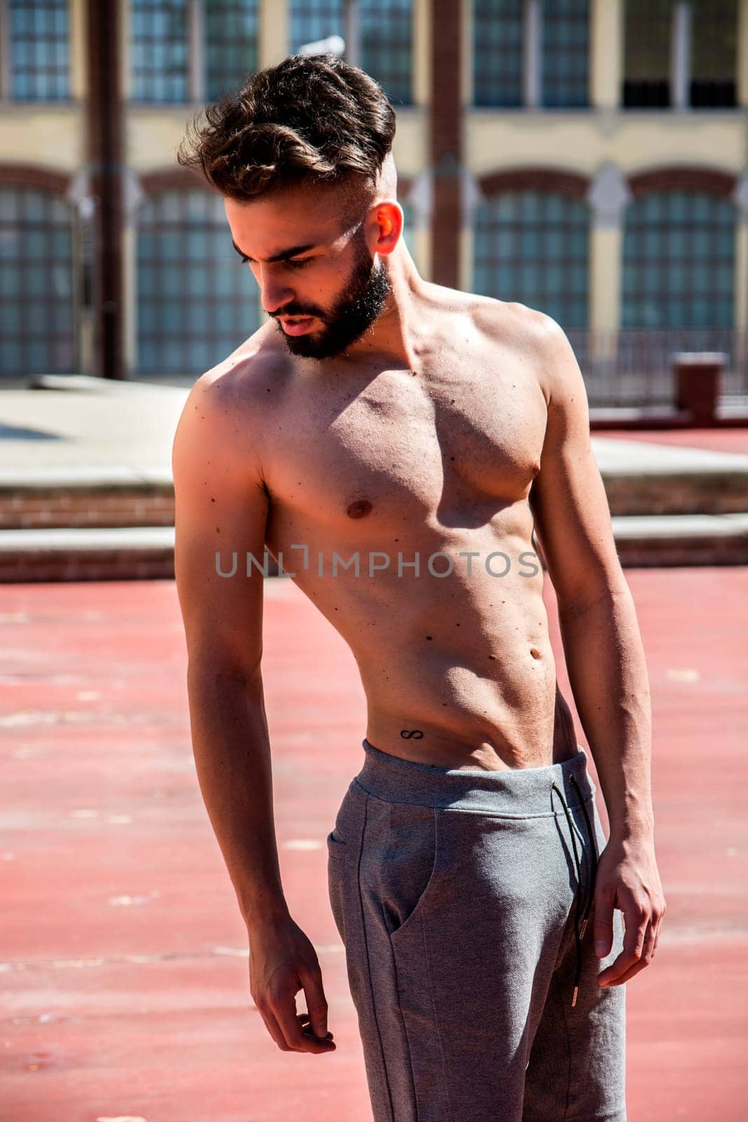 Handsome shirtless young man with beard looking down to a side
