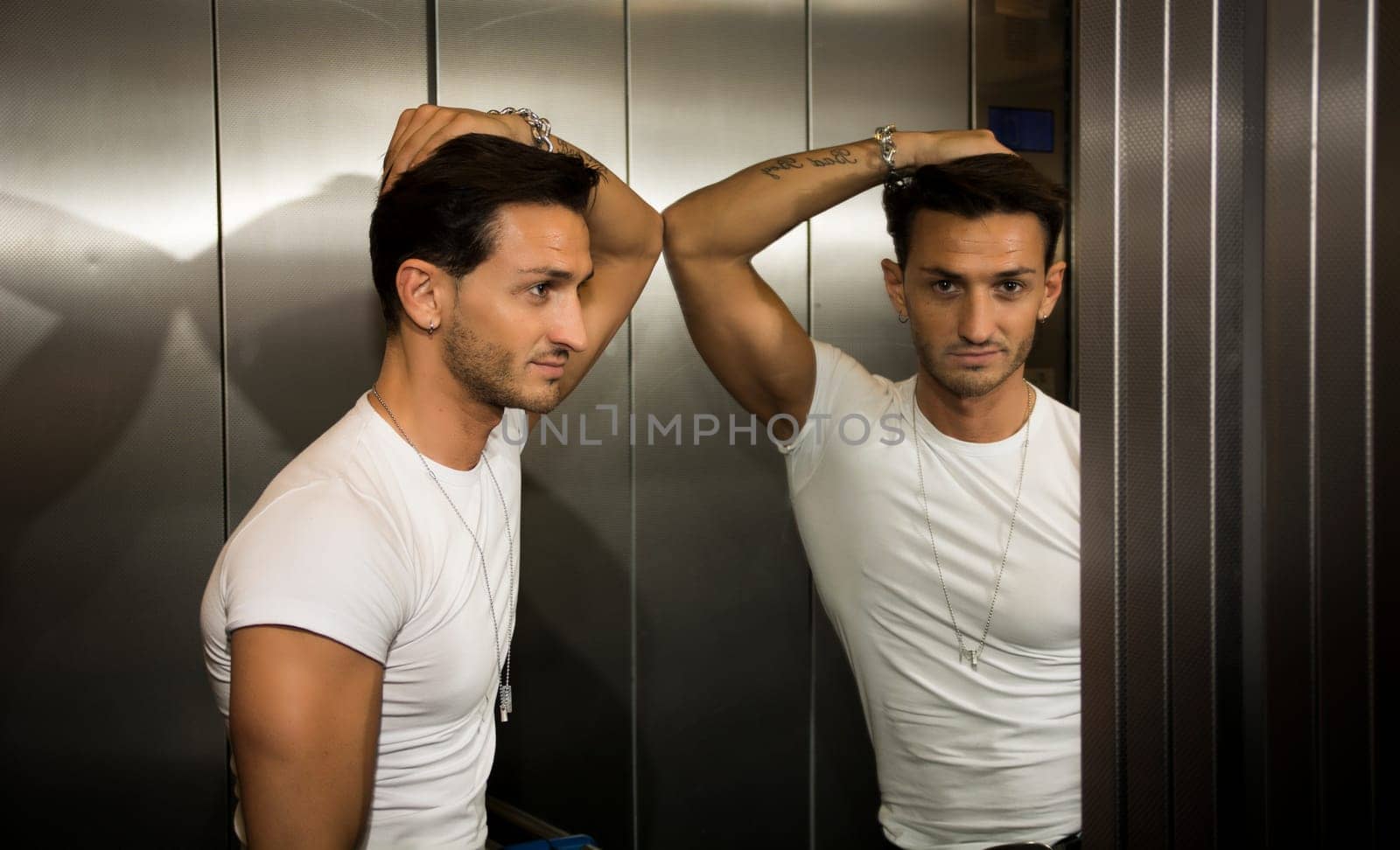 Handsome young man leaning against mirror inside an elevator (lift), looking at camera
