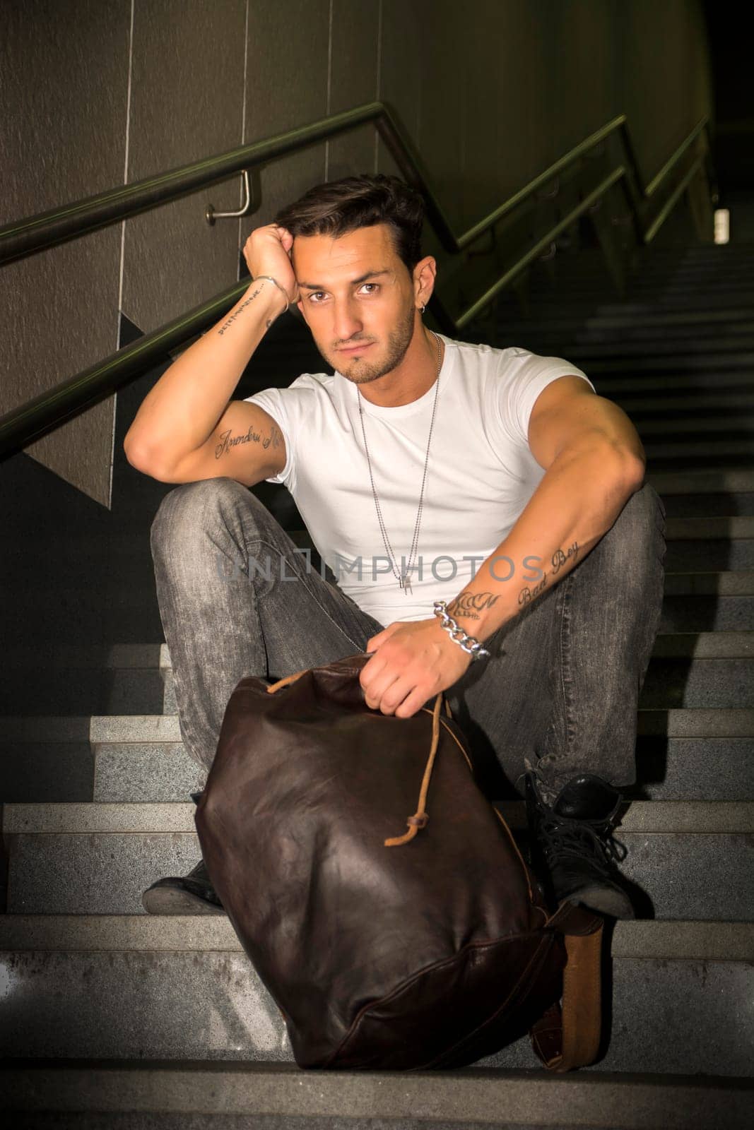 Handsome young man sitting on stairs' granite steps, looking at camera