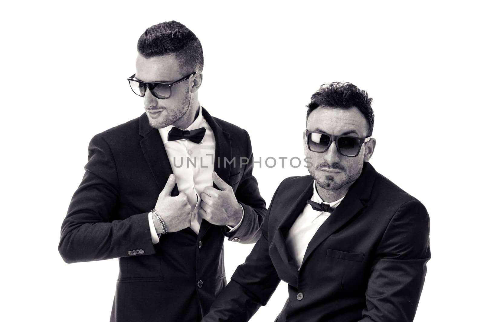 Two elegant men in suit and bowtie isolated on white, one standing, one sitting