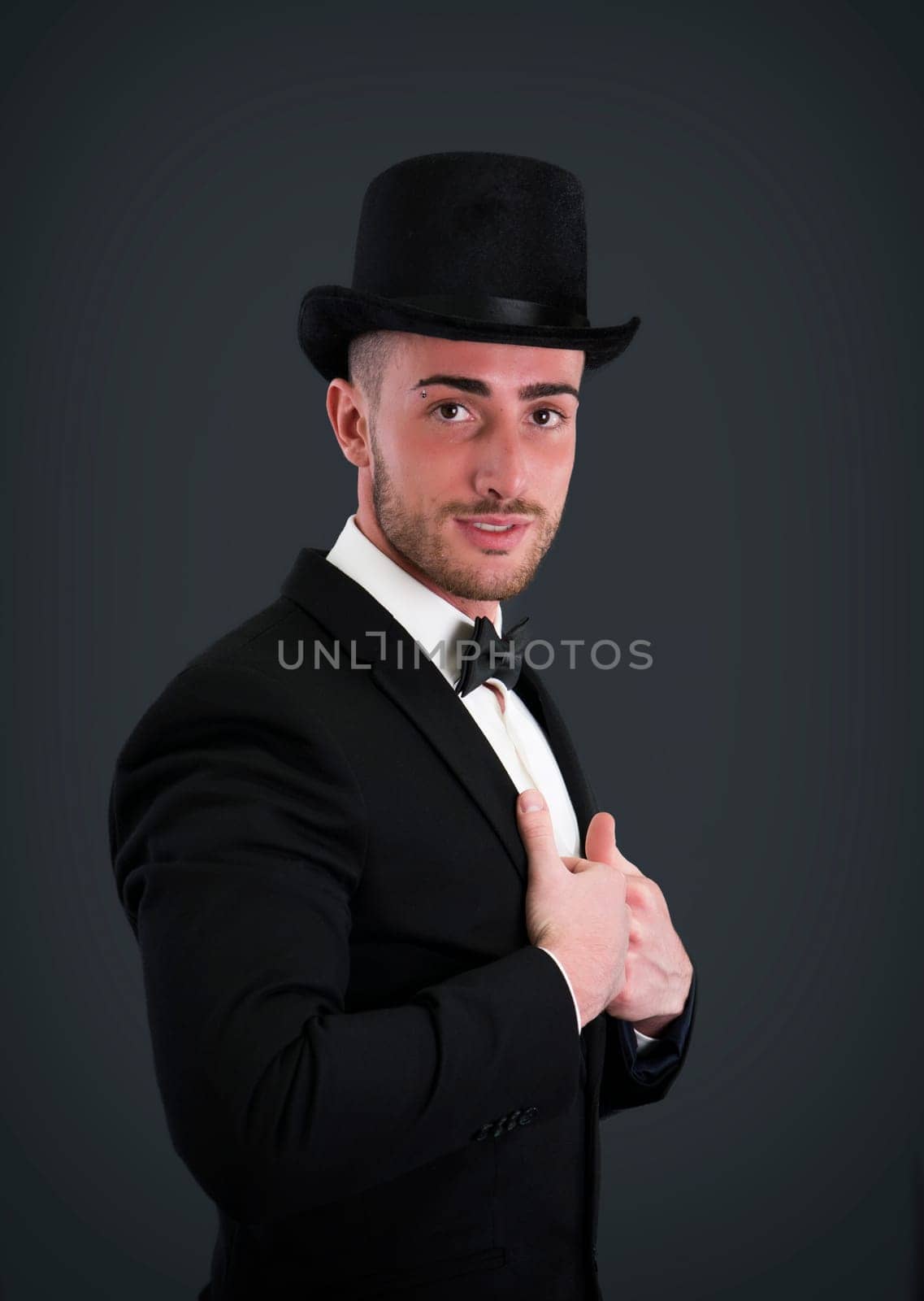 Attractive young businessman with suit, top-hat and bowtie on dark background