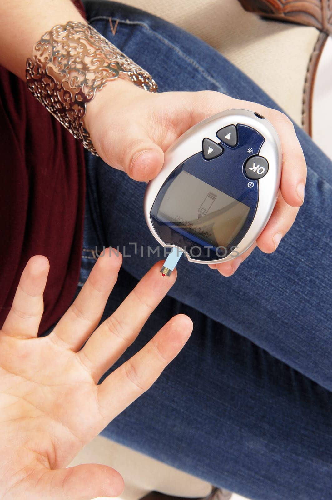 A young woman sitting in jeans testing her bloodsugerlevel with a.instrument.