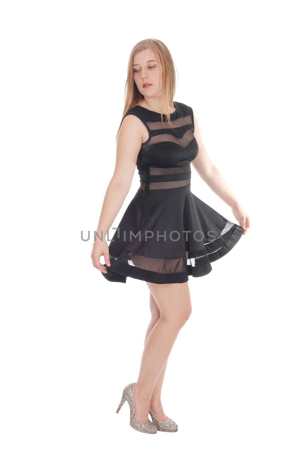 A beautiful young woman standing in a short black dress and high.heels, looking away, isolated for white background.