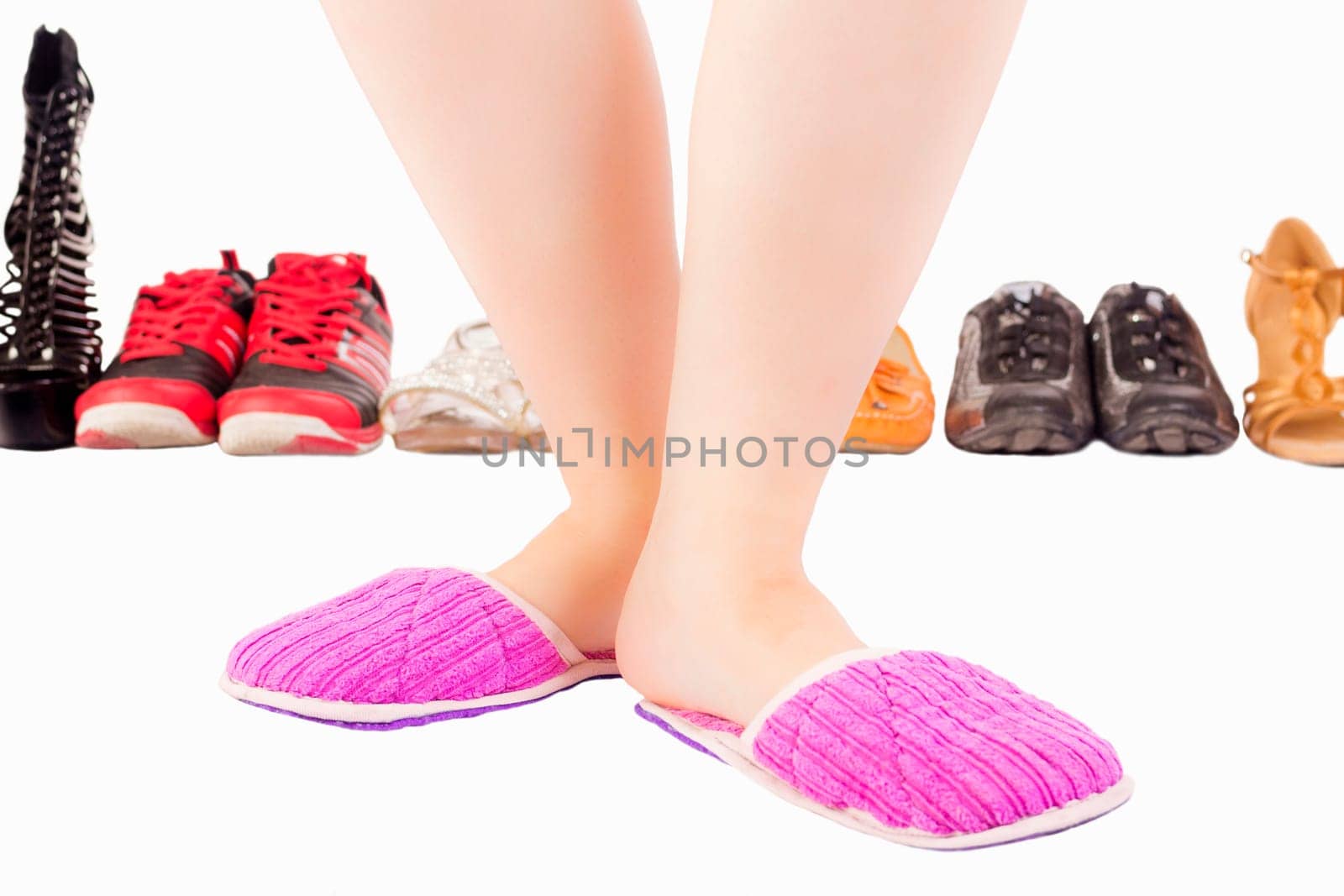 Female legs in pink slippers on white background with different shoes and footwear.