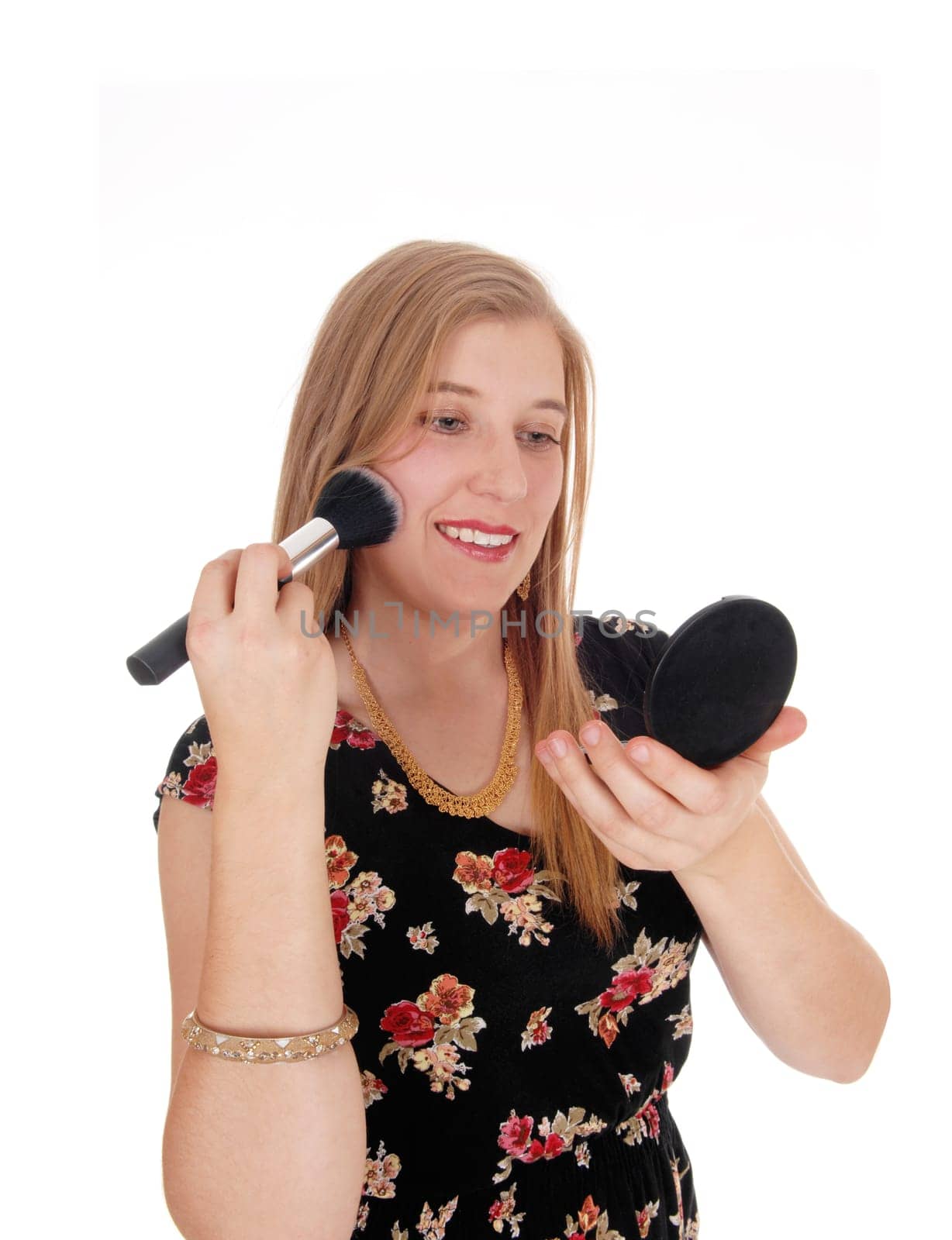 A gorgeous lovely woman standing in a dress holding her little.mirror and putting on makeup, isolated for white background.