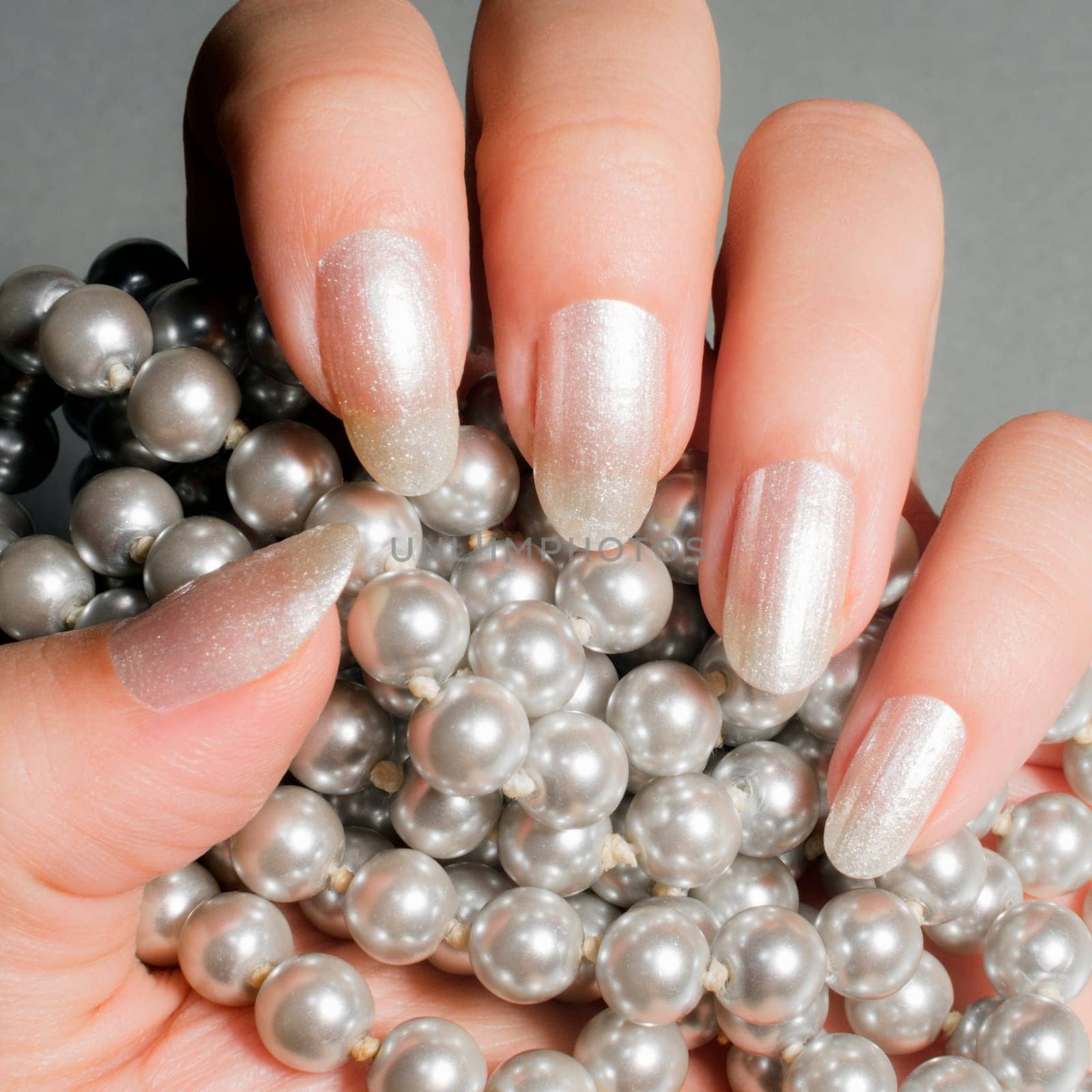 Female hand with glossy white nails holds pearl jewelry.