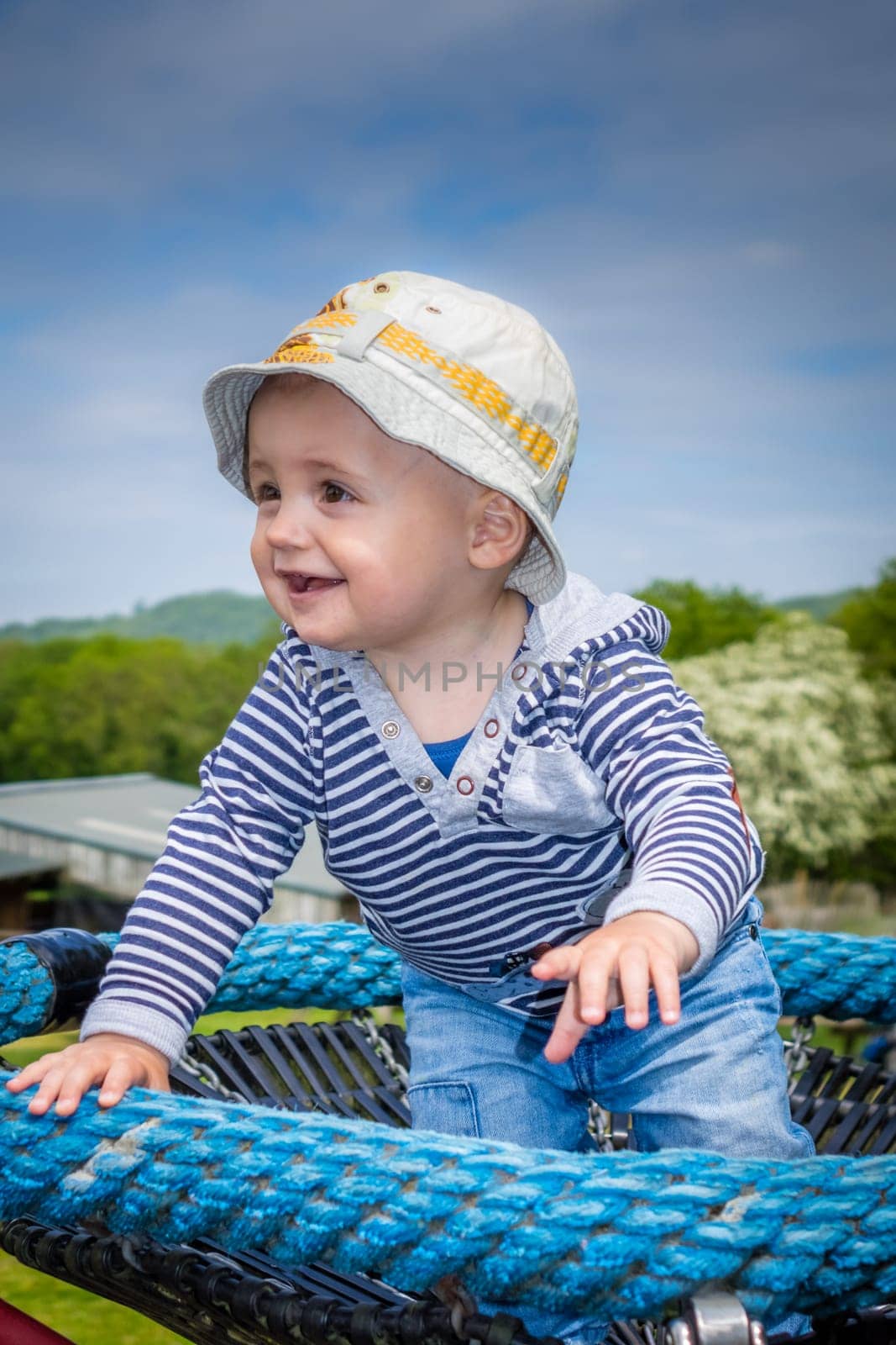 Cute little baby boy standing on a small carousel in the park playground
