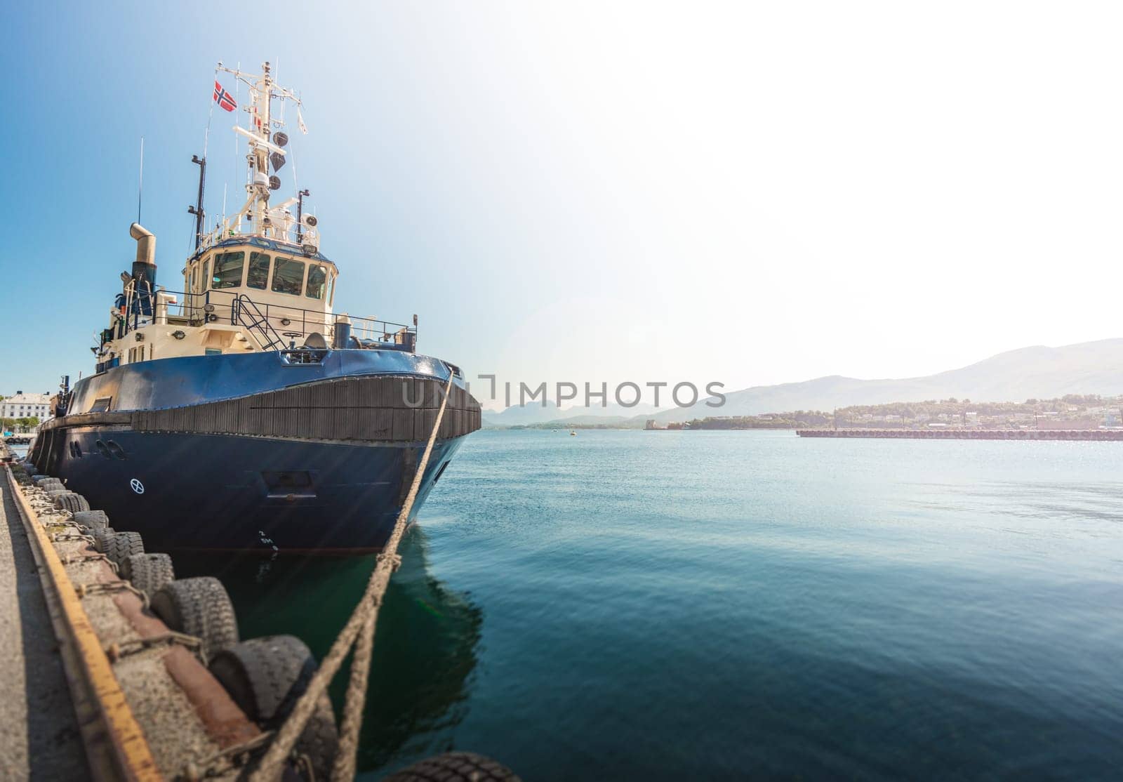 Tugboat or fishing boat in docks of Alesund, Norway, Europe. Ship in foreground and blue sky and mountains in background. Scandinavia travel.