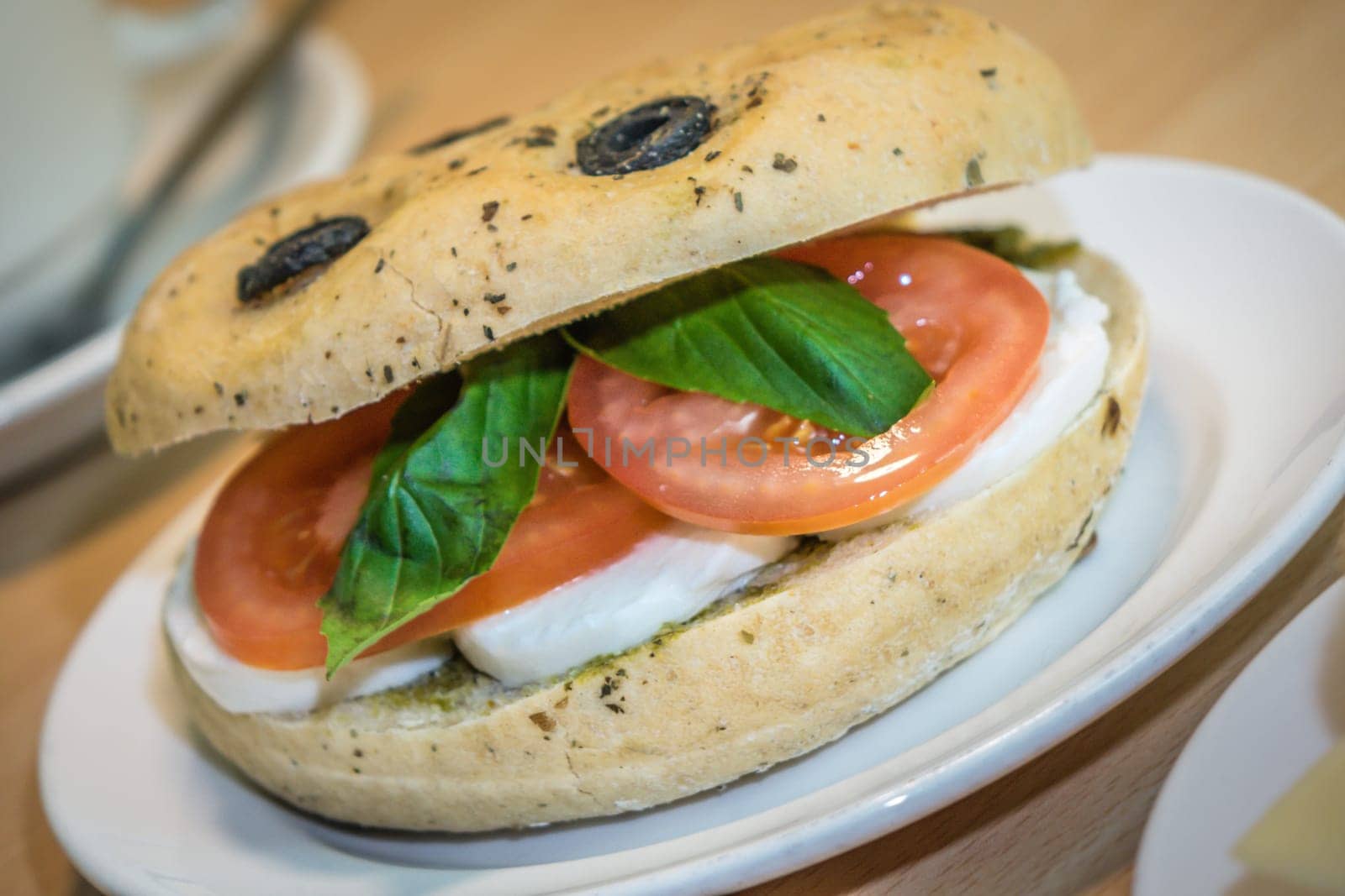 Breakfast bun on a plate, filled with mozzarella, tomato and basil