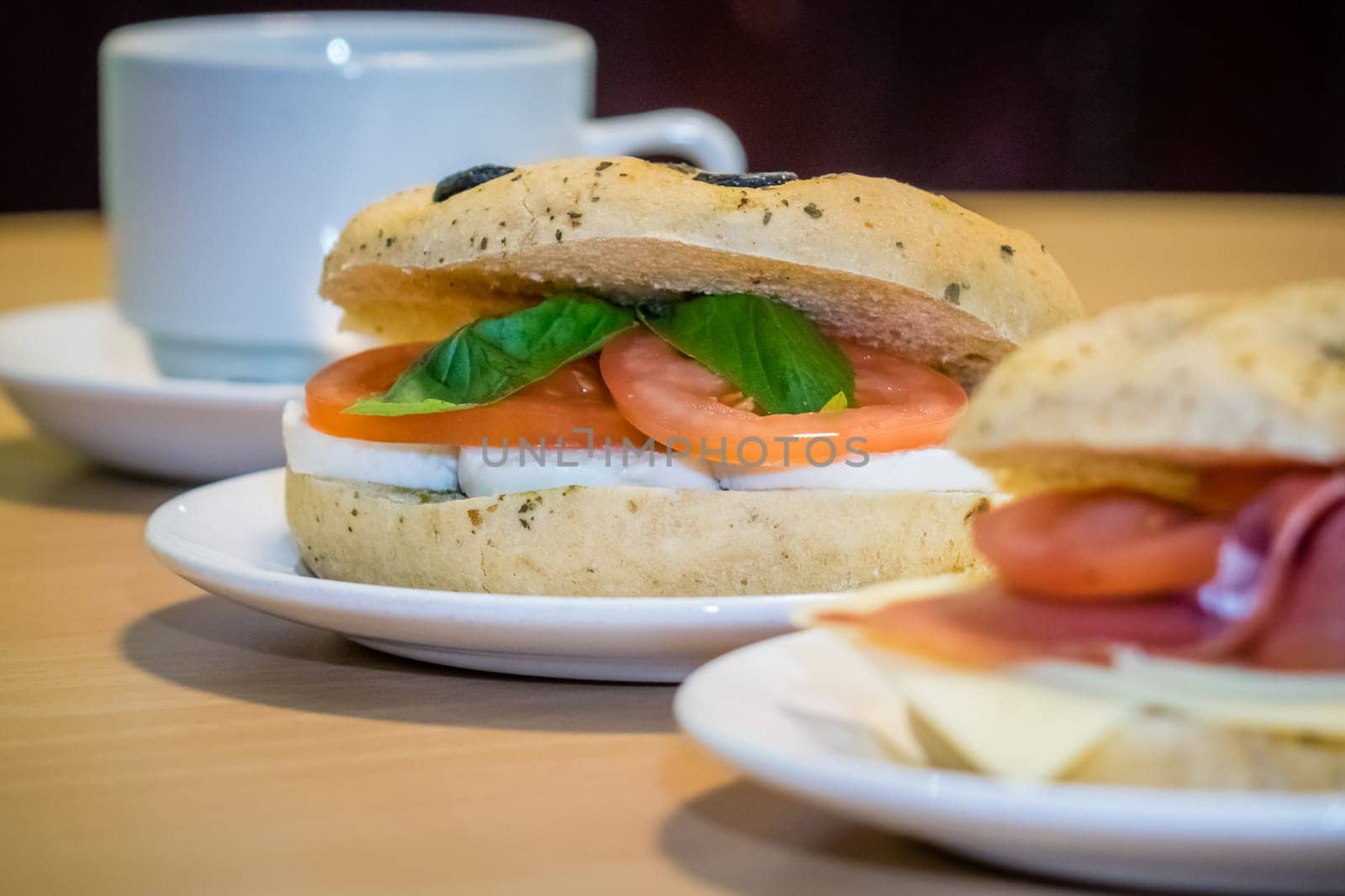 Breakfast bun on a plate, filled with mozzarella, tomato and basil