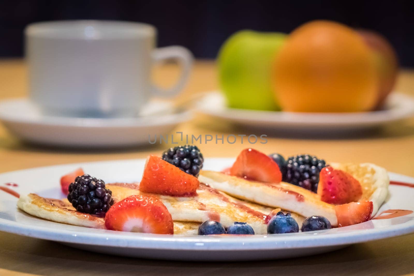 Breakfast meal consisting of pancakes with maple syrup, jam and berries
