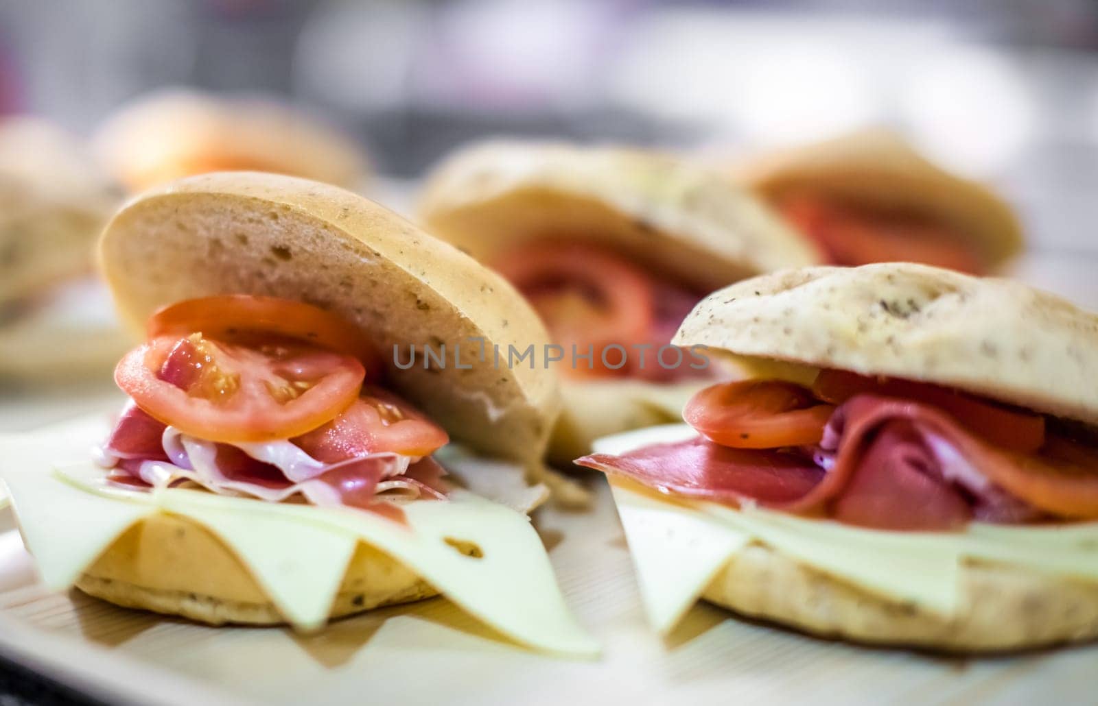Breakfast buns on a plate, filled with cheddar cheese, prosciutto ham and tomatoes