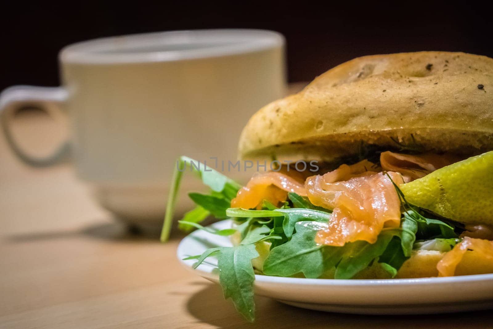Breakfast bun on a plate, filled with smoked salmon and rocket salad