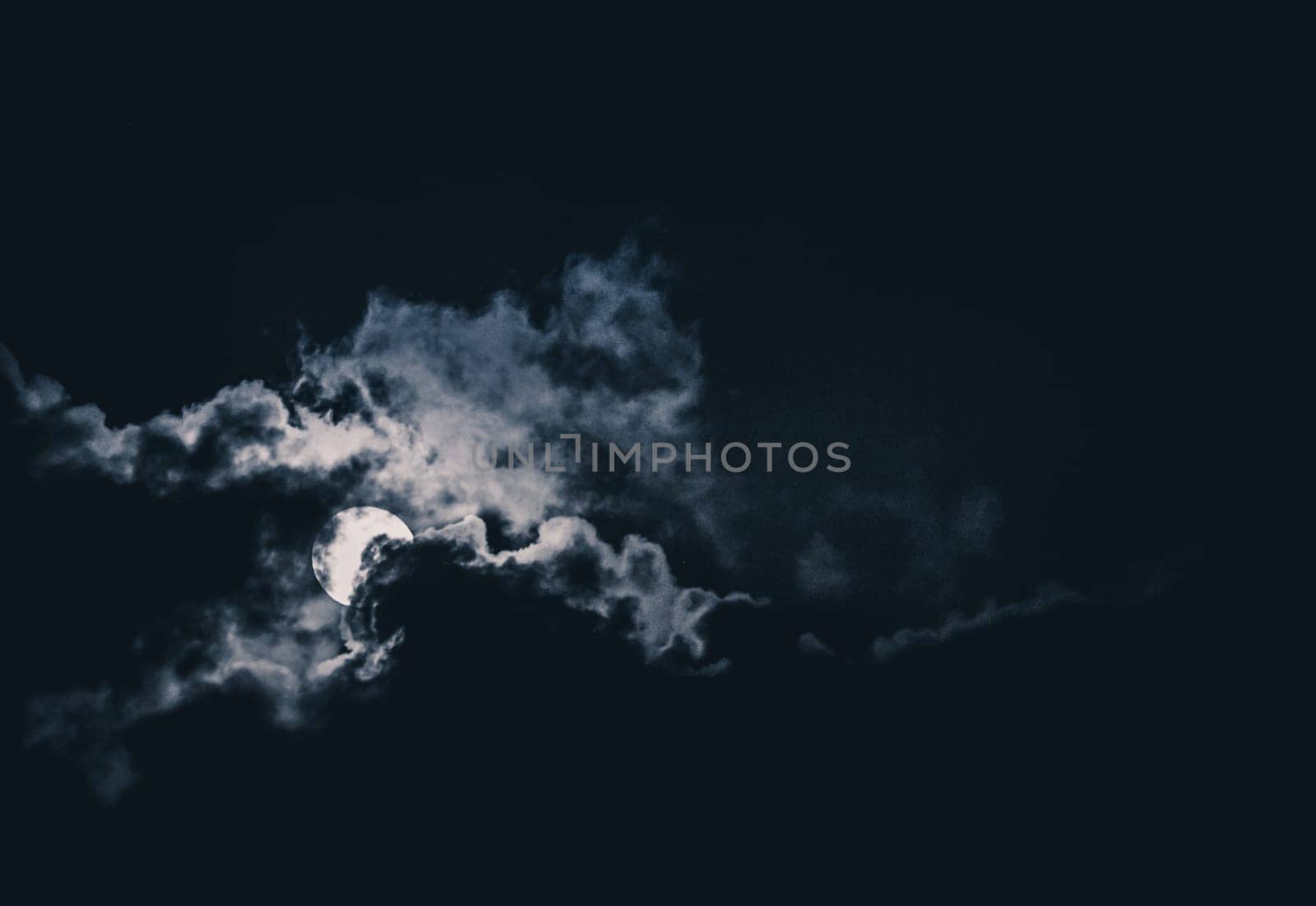 Full moon behind clouds glowing on a dark night sky