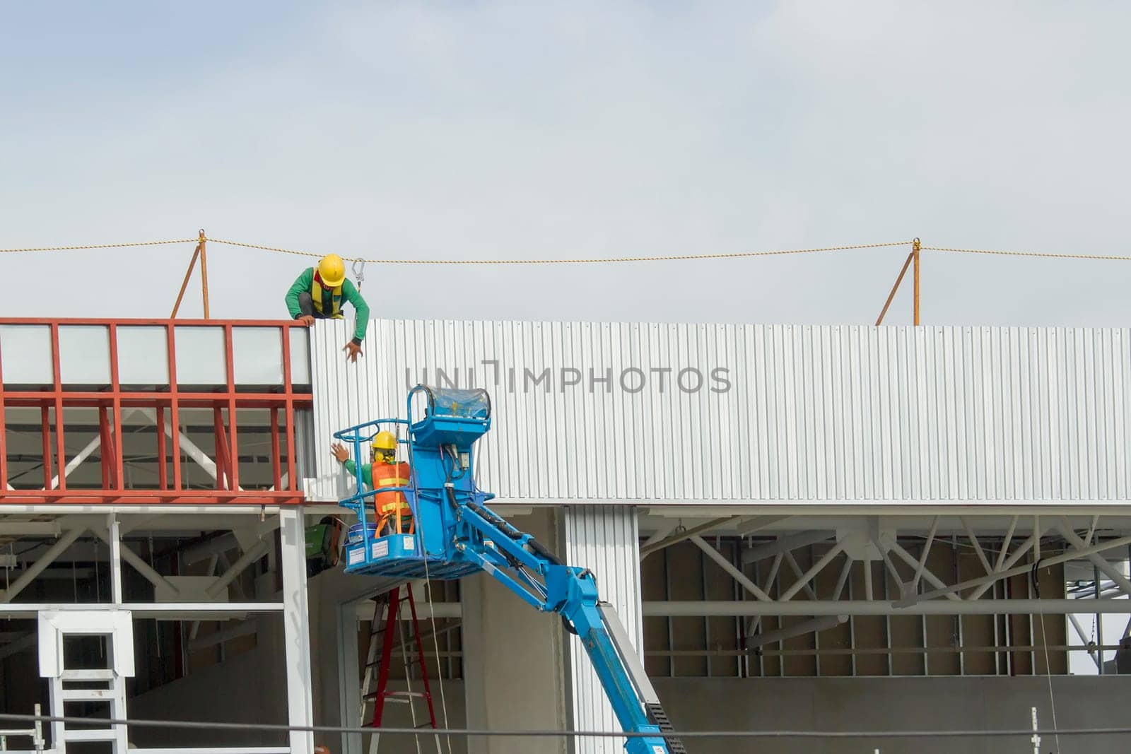 Workers in a baskets are installing sheet, building a factory.