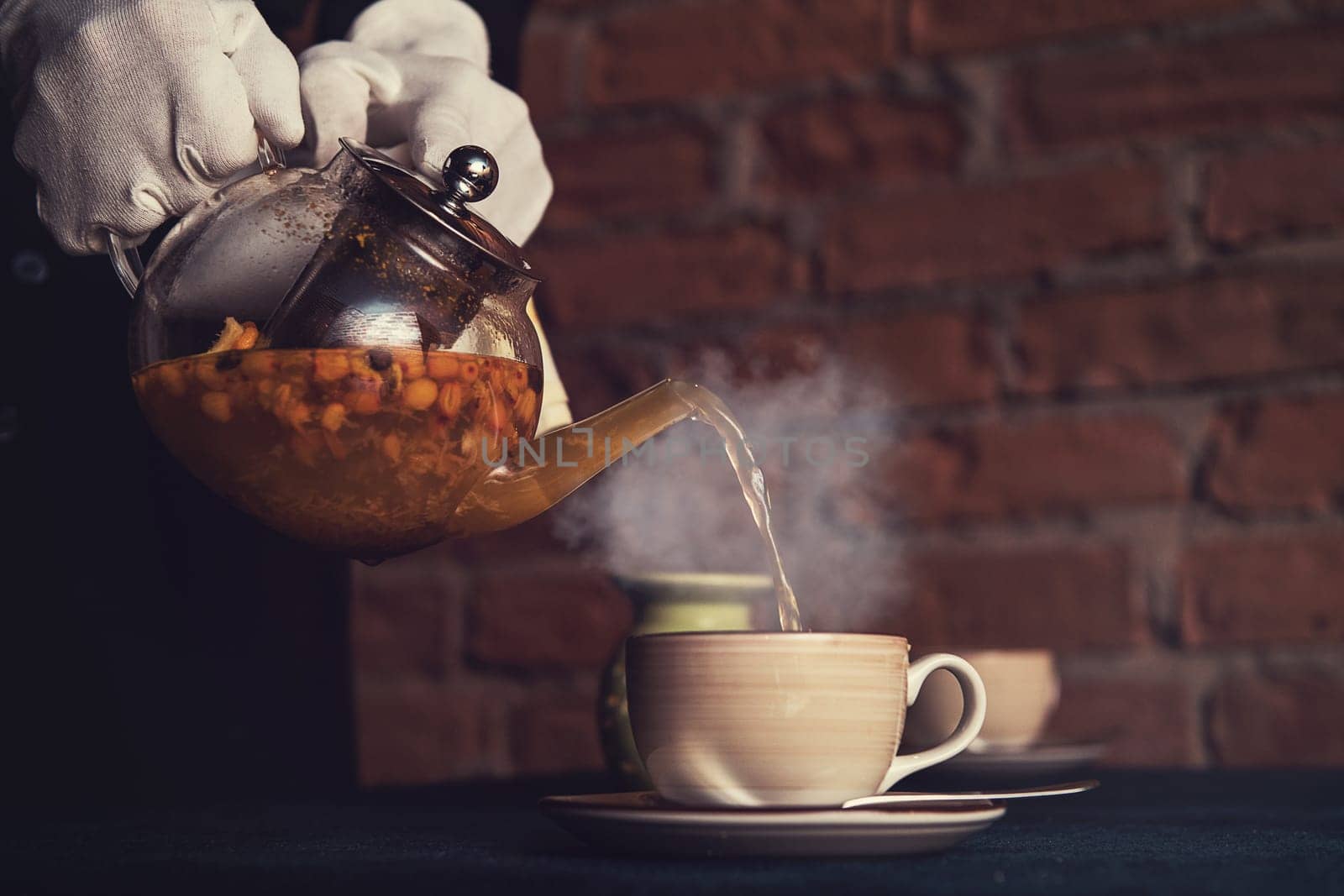 Pouring tea with sea buckthorn honey and herbs in glass teapot