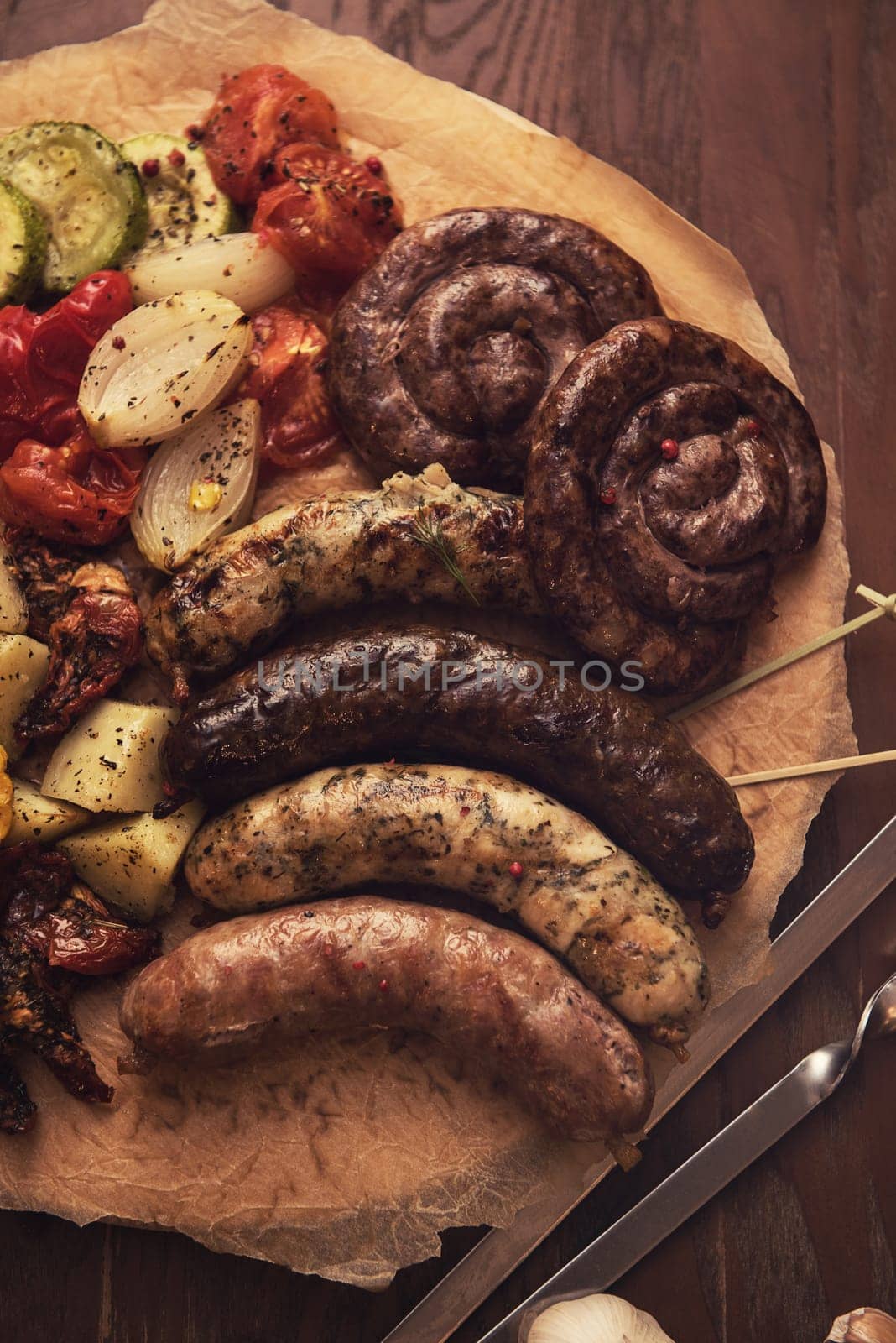 Grilled different meat and fish sausages with vegetables and spices on wooden background