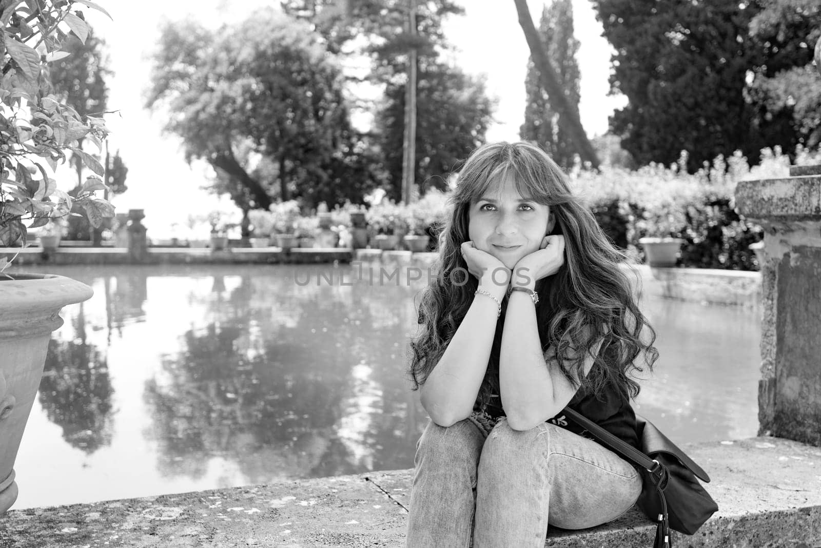 Nice girl with long hair posing near an artificial lake and a lemon tree