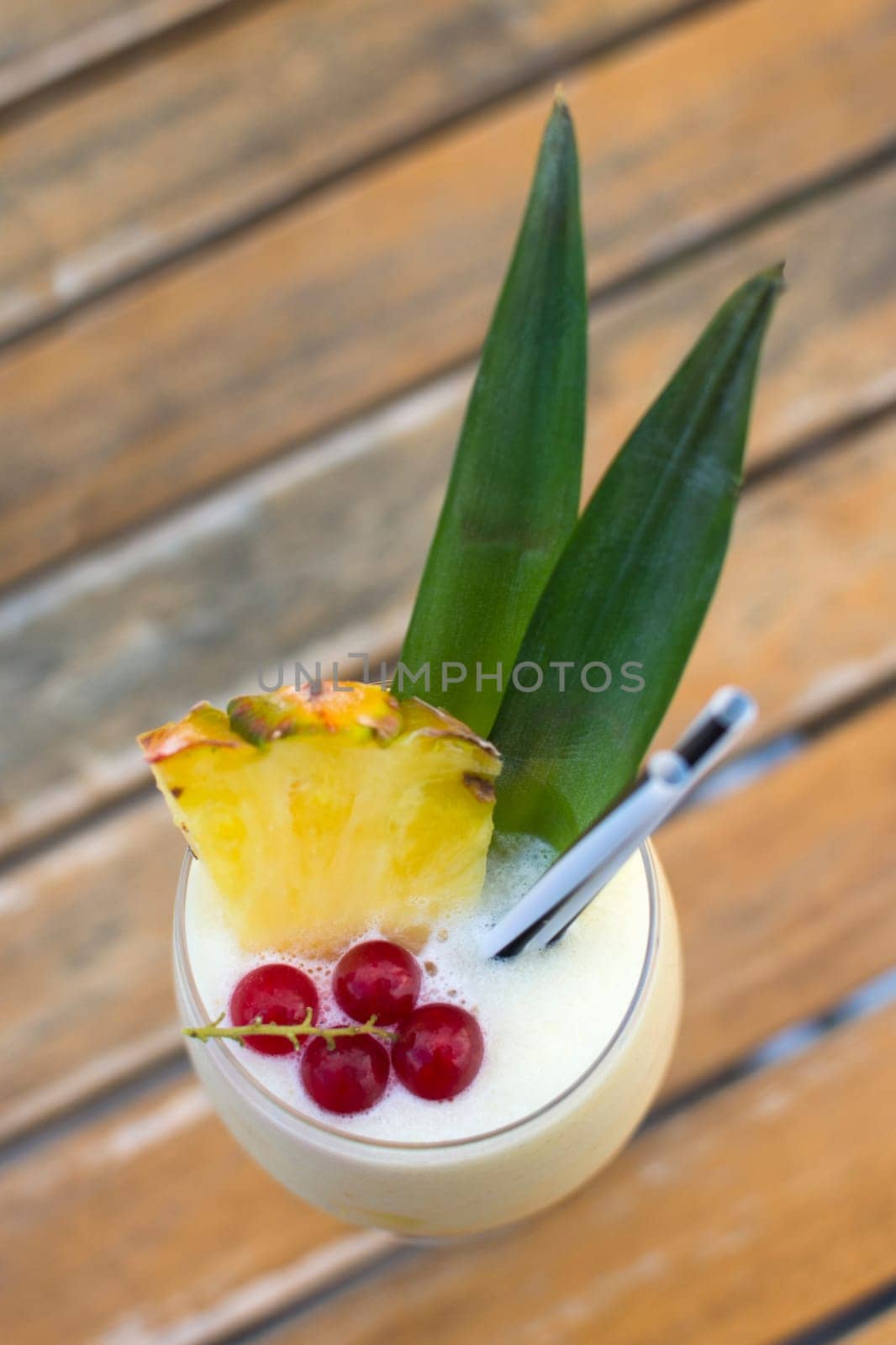 Fruit cocktail with alcohol, pineapple and red currant on wooden table.