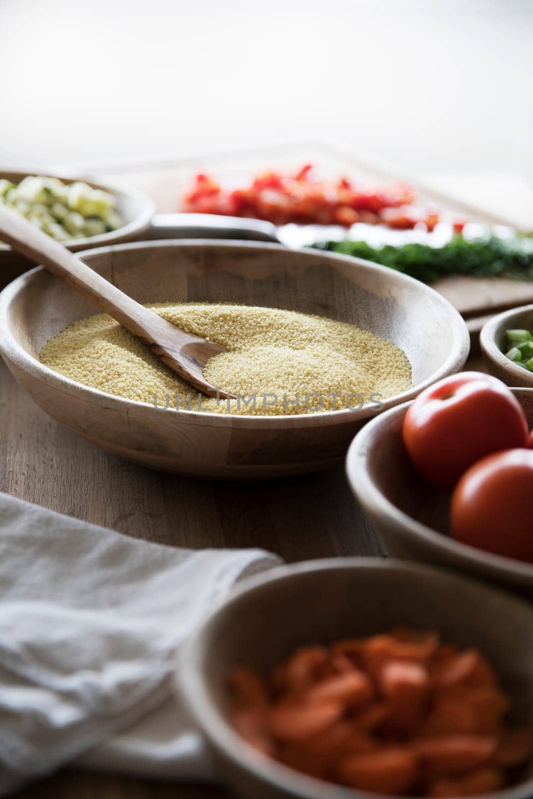 Couscous in wooden bowl on table with other ingredients.