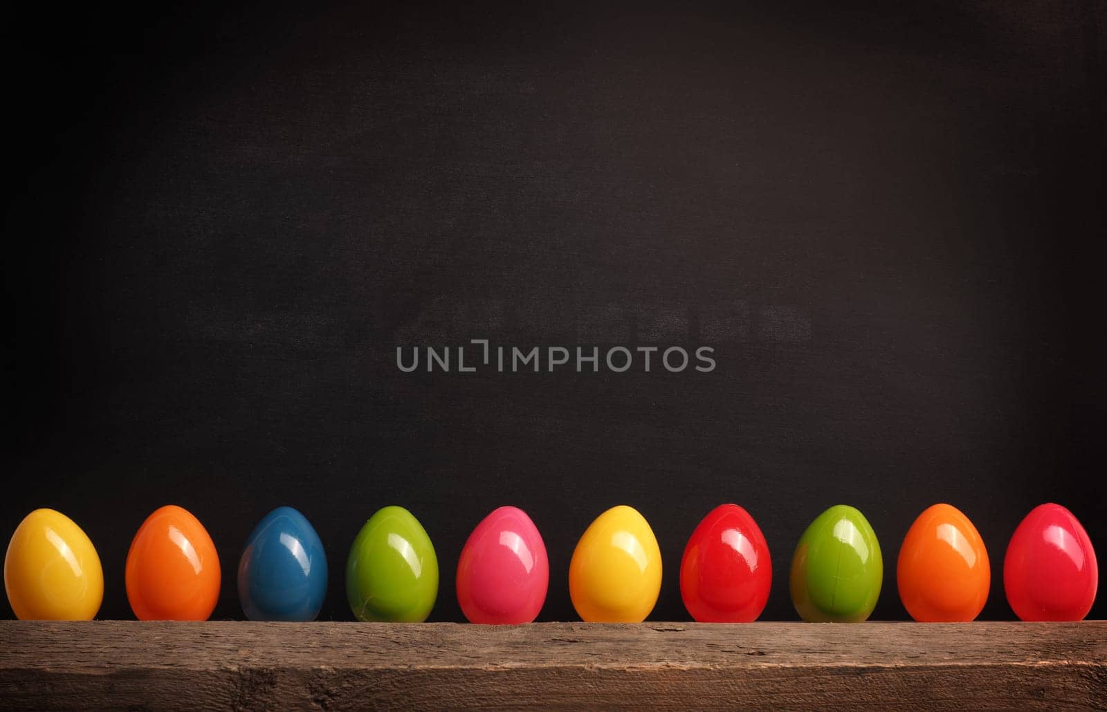 Colorful plastic Easter eggs in row on a black chalkboard with space for text or image