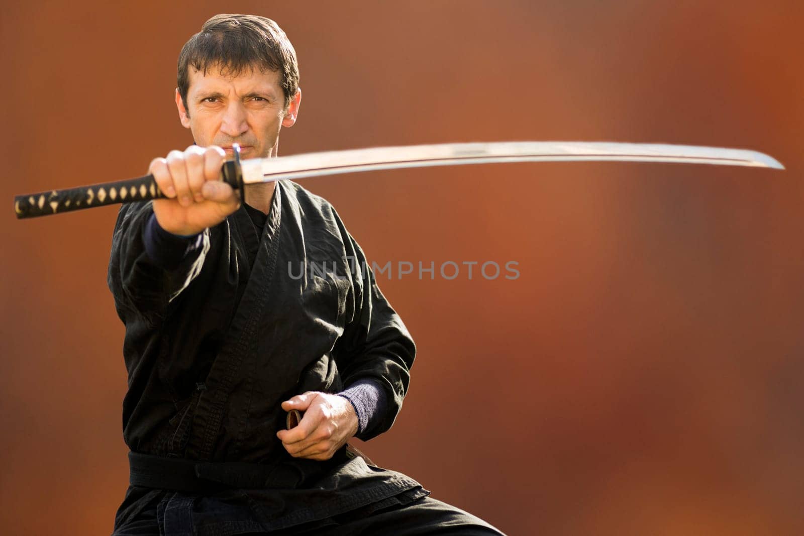 Sitting ninja in black kimono is holding his sword on brown background.