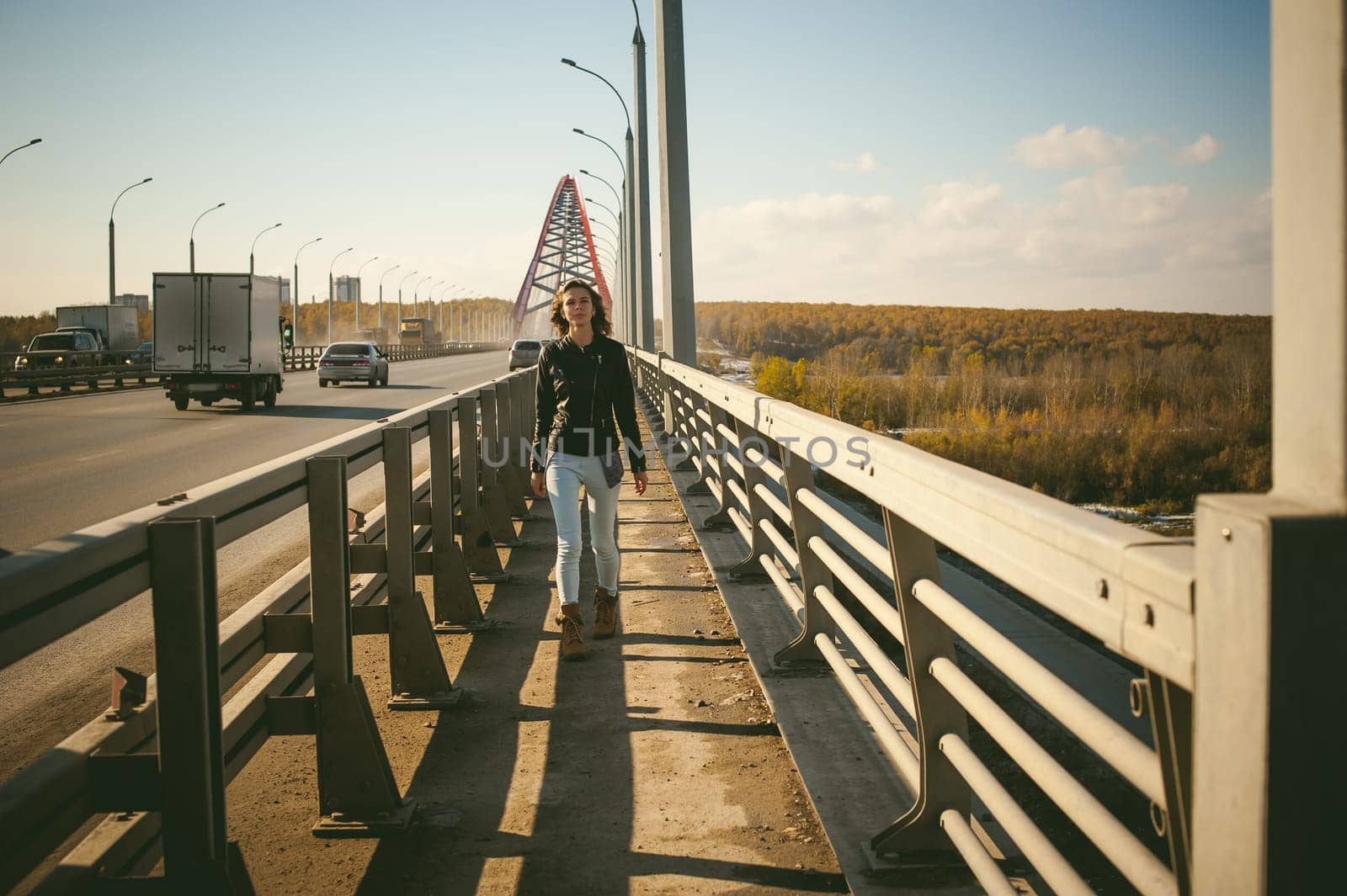 girl goes on road bridge. lonely young woman in black Leather jacket autumn, walking over the bridge which goes transport.