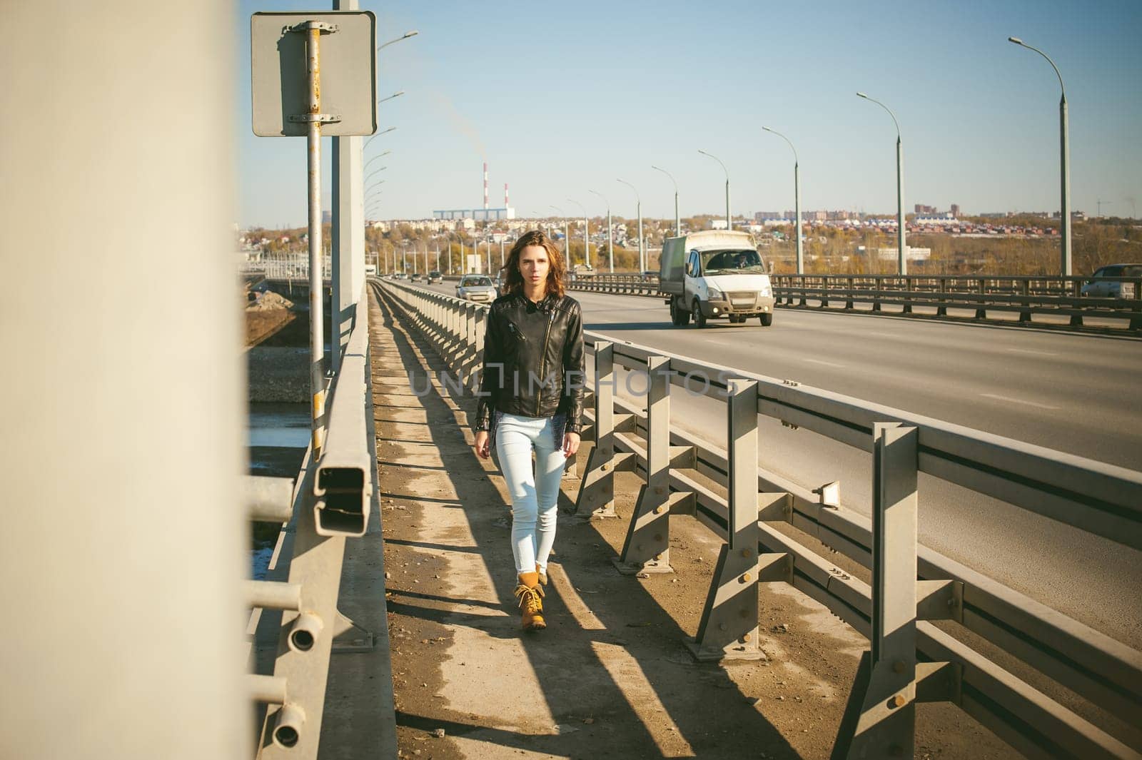 girl goes on road bridge. lonely young woman in black Leather jacket autumn, walking over the bridge which goes transport.