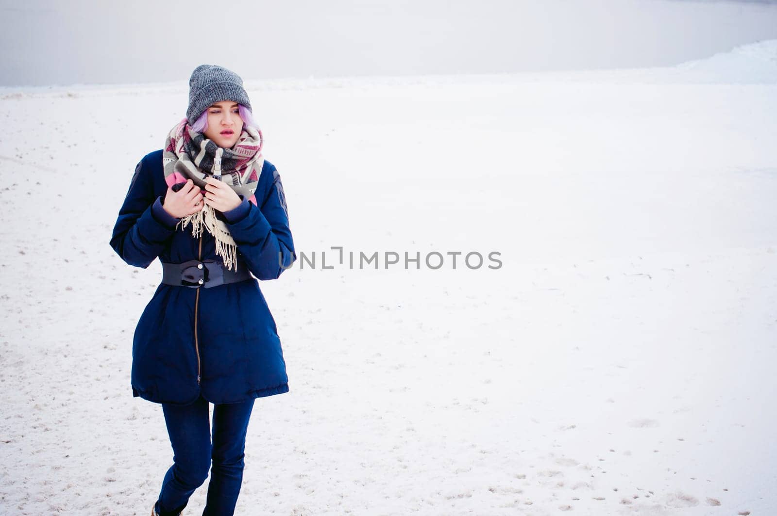 vaping girl. winter street portrait of a woman hipster, purple-dyed hair, a gray knitted hat and scarf. woman smokes an electronic cigarette in the street near the snow-covered river