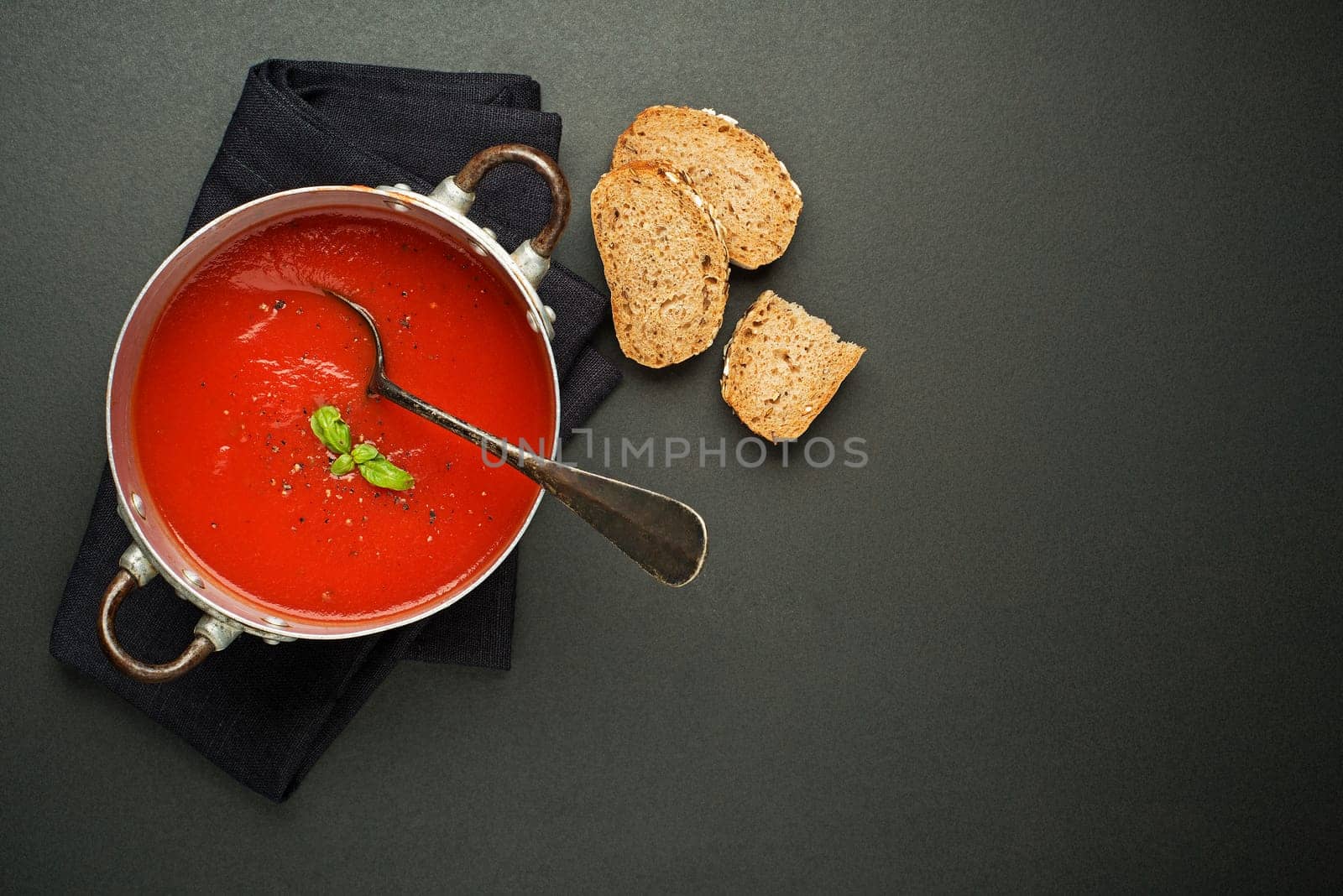 Fresh tomato soup with bread on black background. Top view