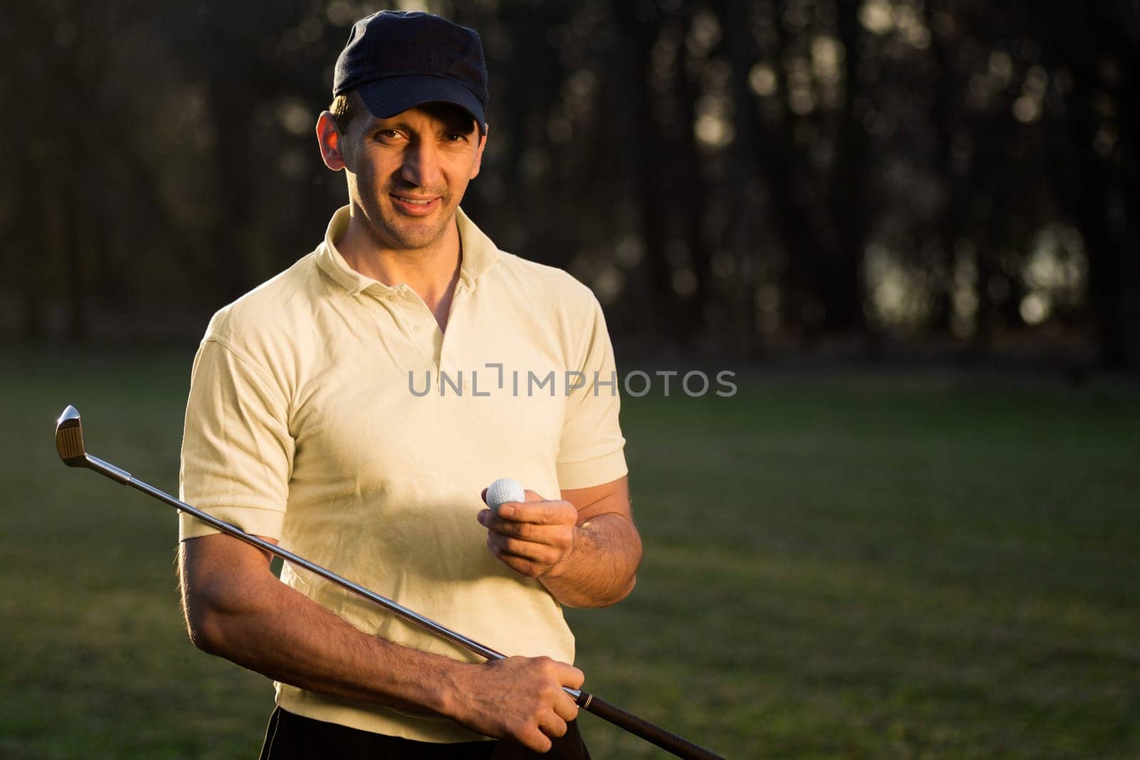 Handsome smiling golfer is holding a golf ball and the putter.