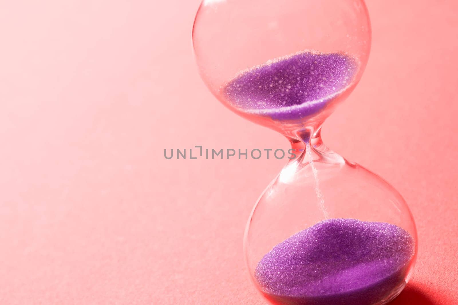 Purple sand clock hourglass on pink background, out of time concept.