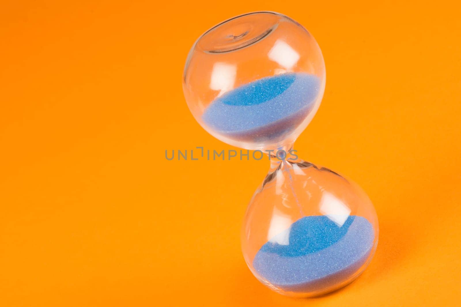 Blue sand clock hourglass on orange background, out of time concept.