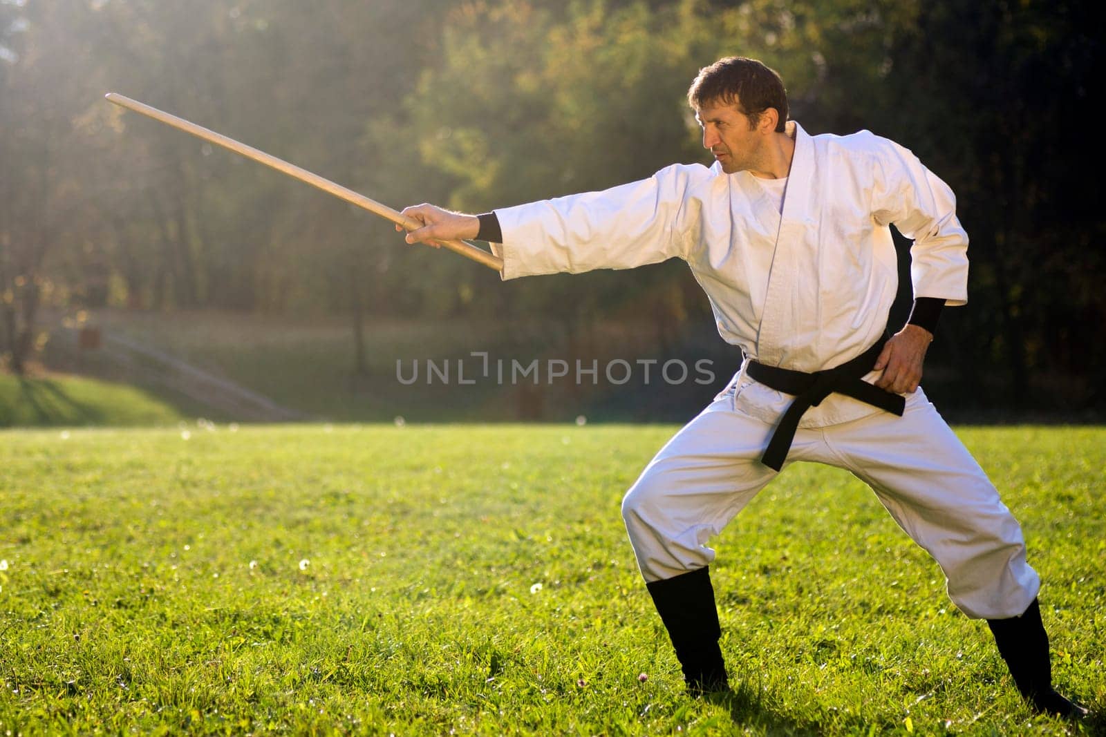 Man in white kimono is practicing with wooden sword outdoors in the park.