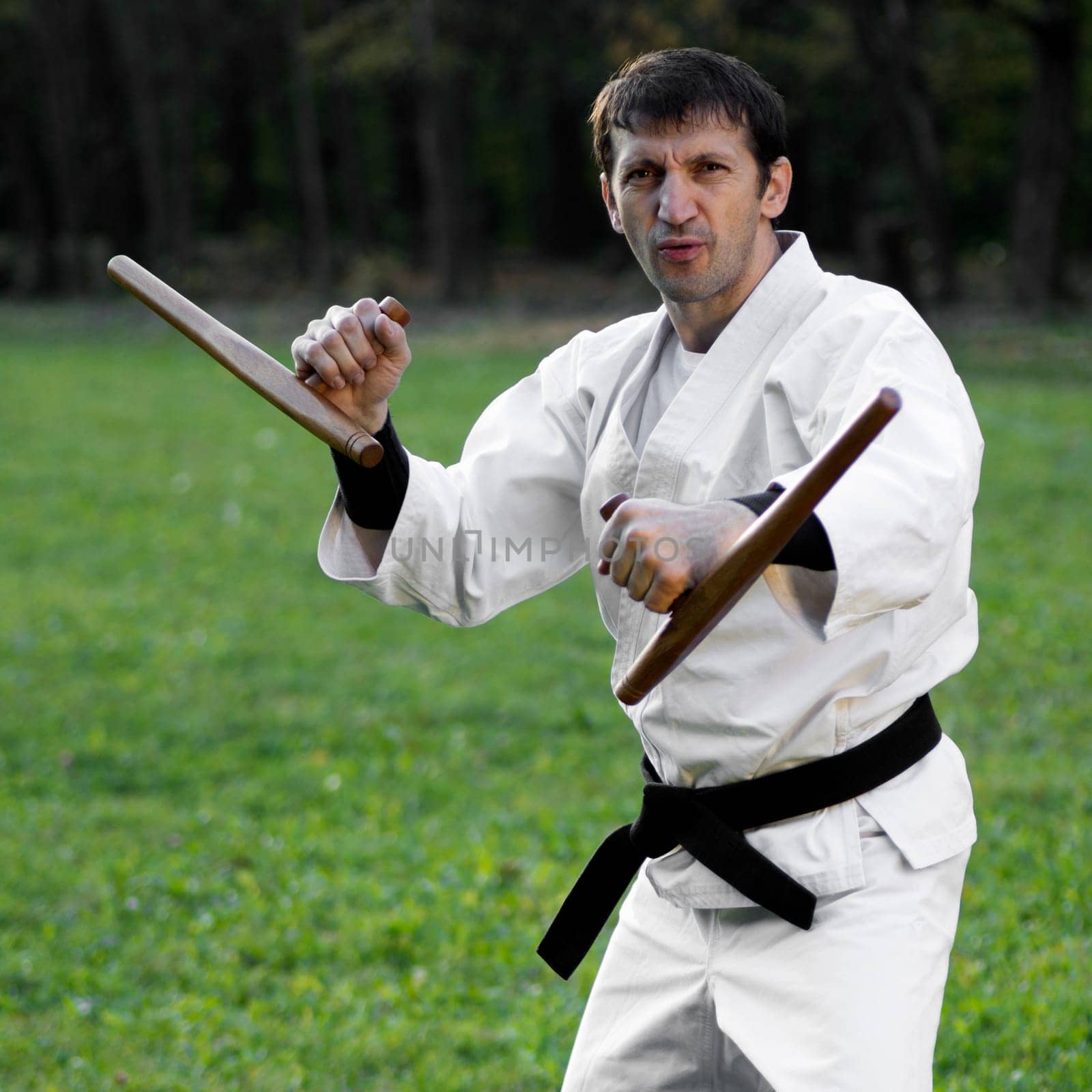Master of martial arts in white kimono is practicing with tonfa.