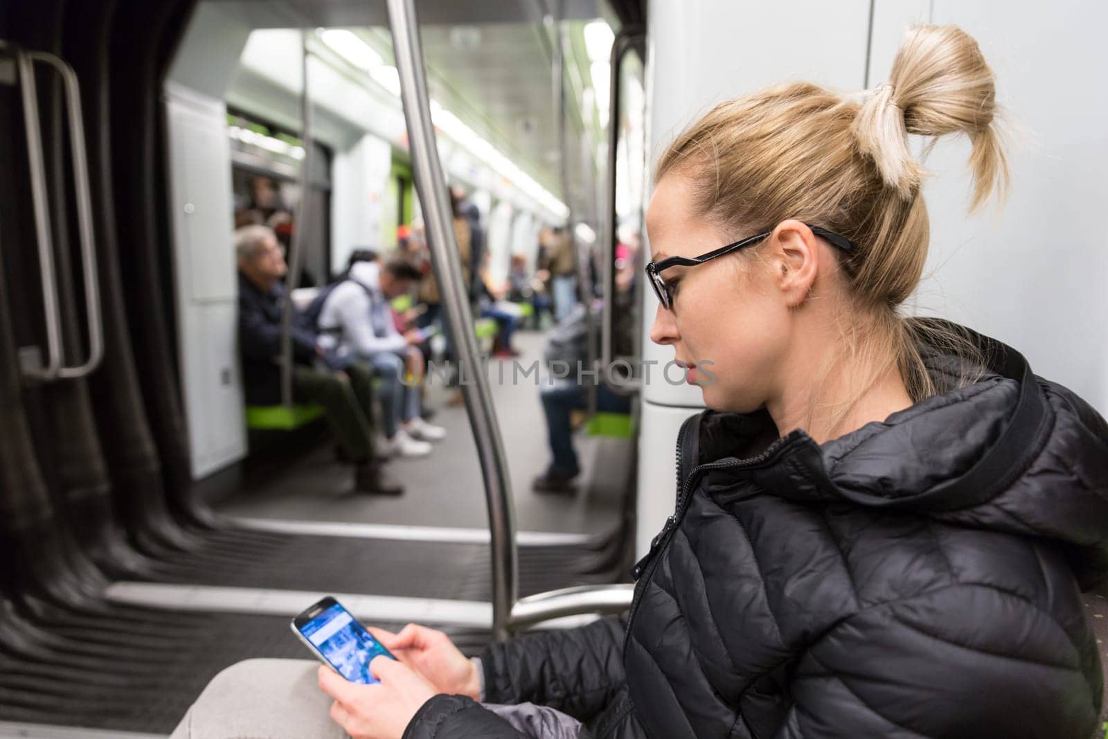 Cheerful young girl texting on mobile phone social network applications while traveling on metro. Wireless internet on public transport concept.