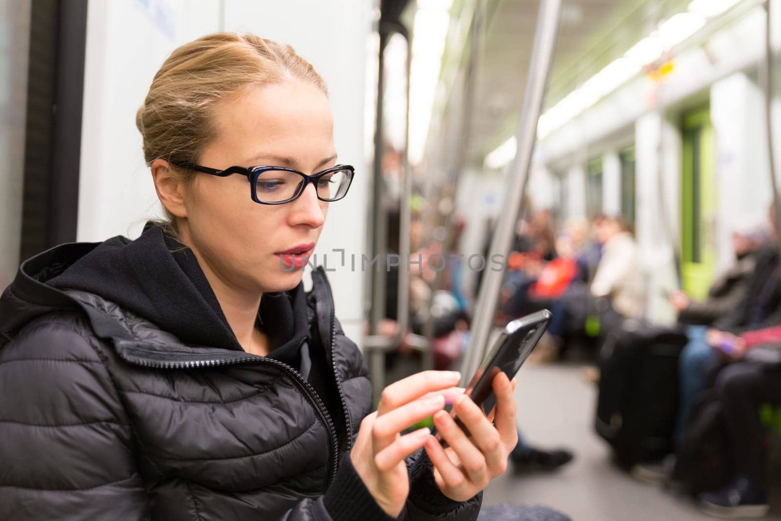 Young girl reading from mobile phone screen while traveling on metro. Wireless internet on public transport concept.