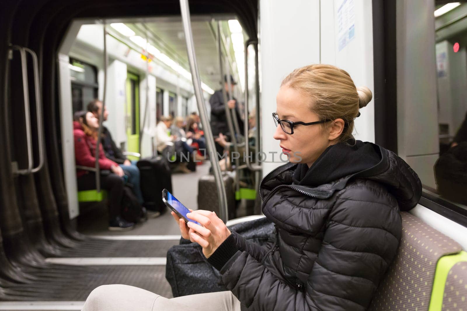 Cheerful young girl texting on mobile phone social network applications while traveling on metro. Wireless internet on public transport concept.