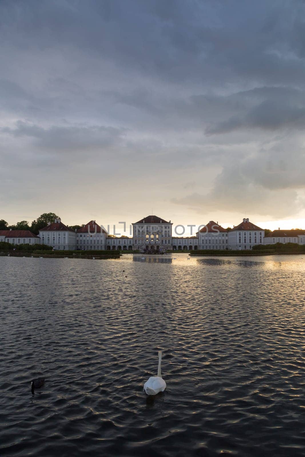 Dramatic scenery of Nymphenburg palace in Munich Germany. Sunset after the sorm. White swan swimming in pond in front of the palace.