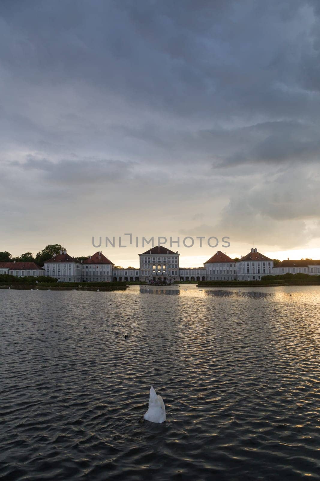 Dramatic scenery of Nymphenburg palace in Munich Germany. Sunset after the sorm. White swan diving in pond in front of the palace.