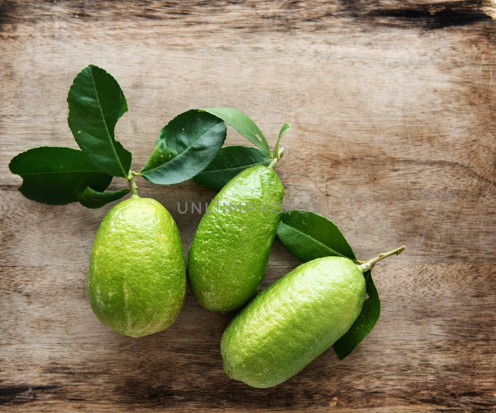 Top view pesticide free fresh organic lemons with leaves on wooden table background, imperfect insect bites.