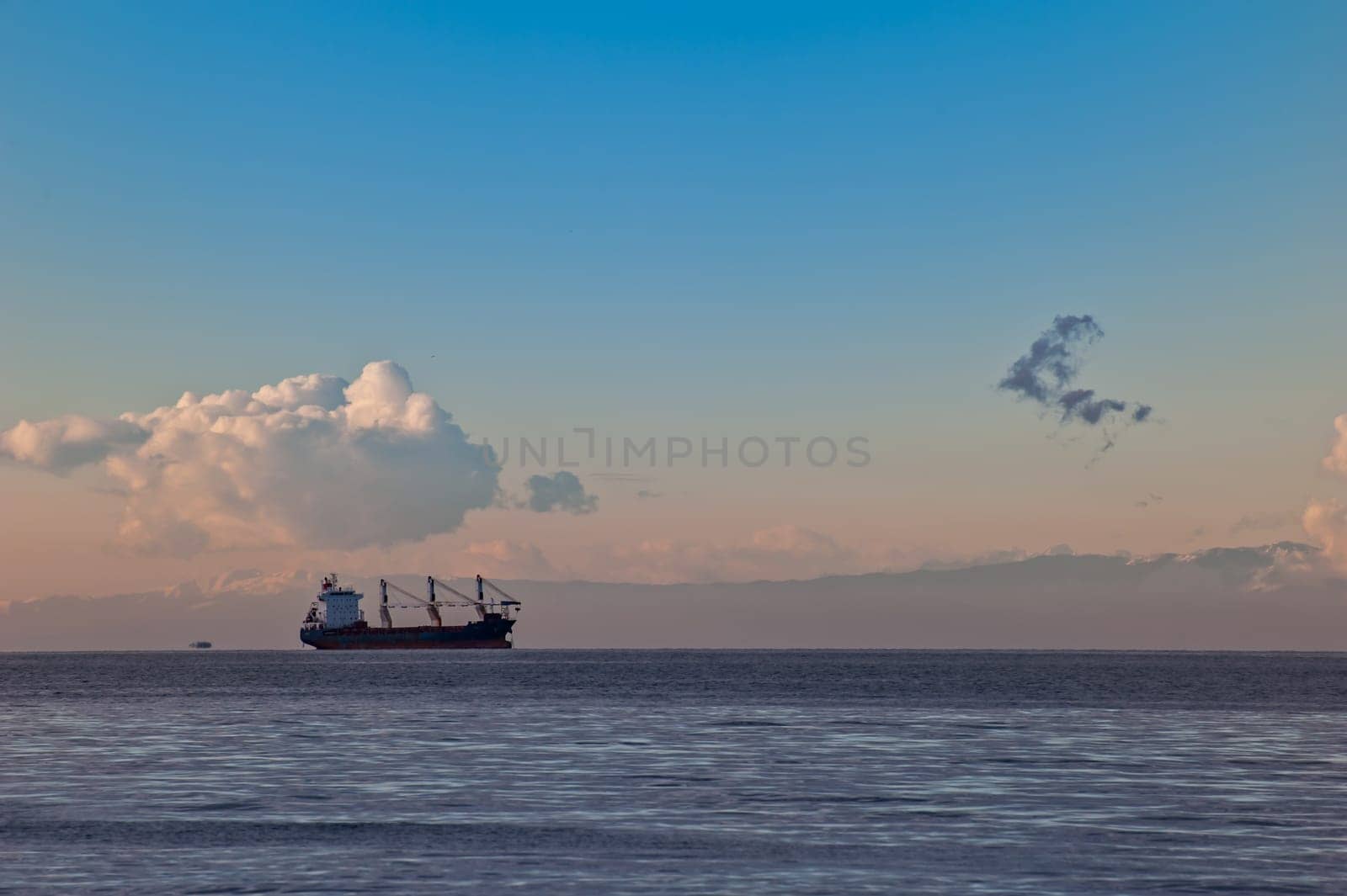 Seascape with ship at sunset with clouds. Mountains in background.