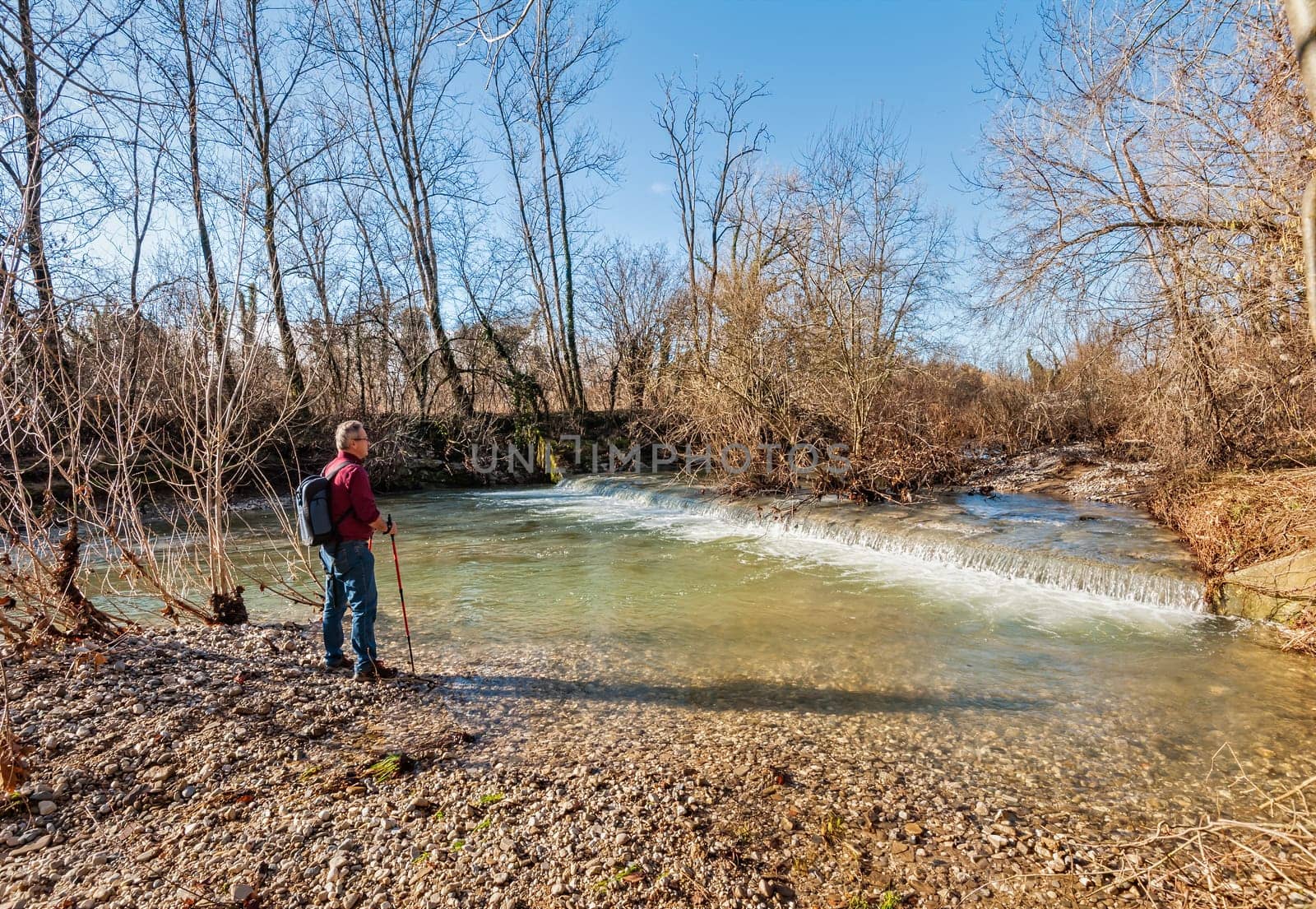 Hiker of about 60 years, on the bank of the stream overlooking a small waterfall.