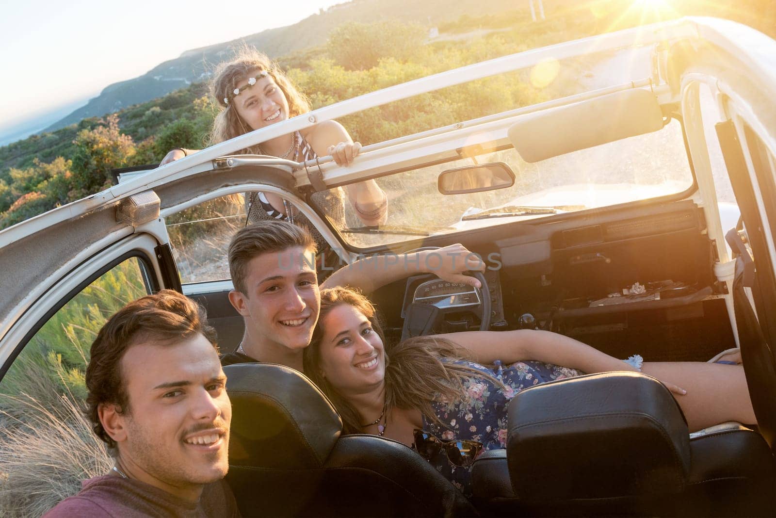 Group of happy people in a car at sunset in summer.
