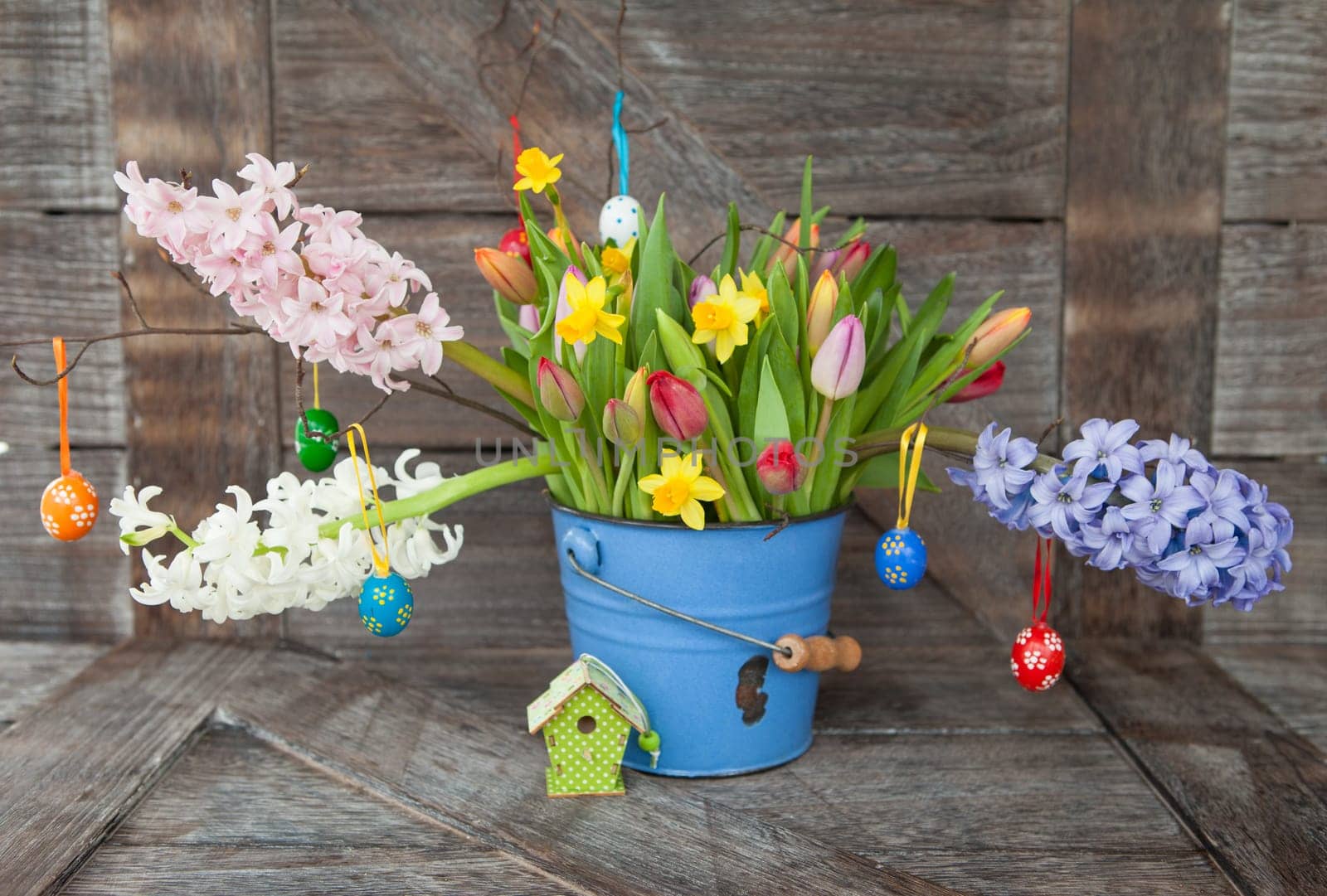 Colorful spring flowers in blue bucket on background of rustic wood