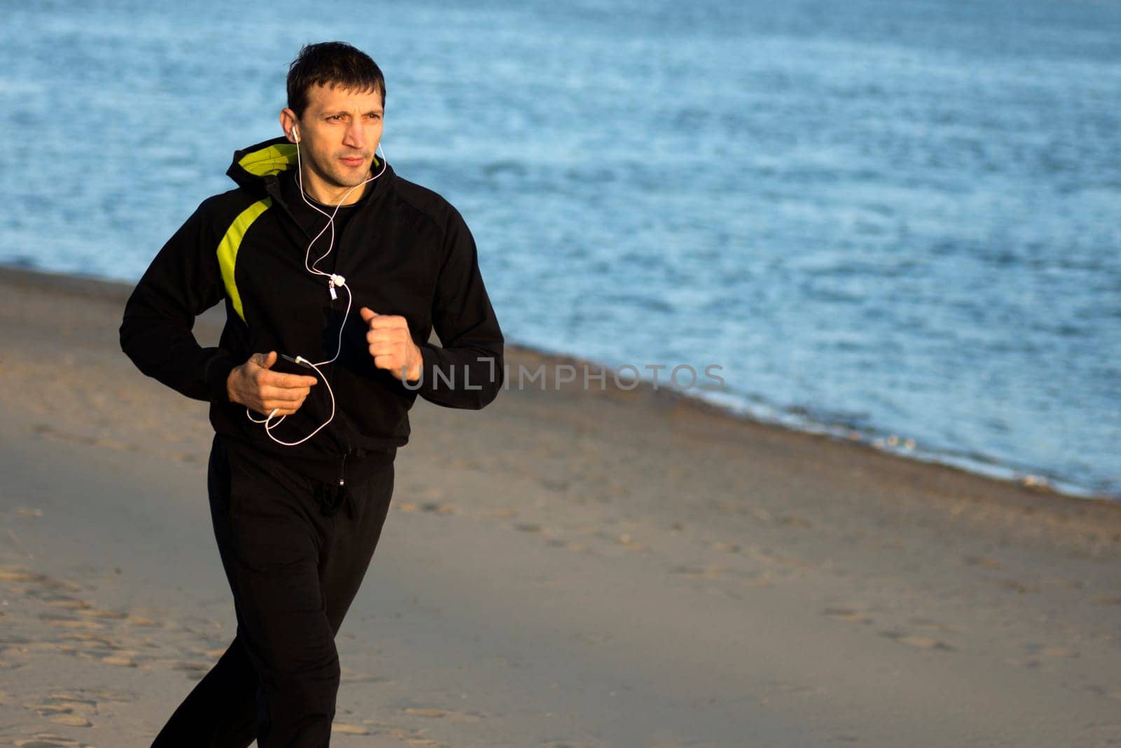 The man in sportswear with earphones is jogging outdoors on the beach.