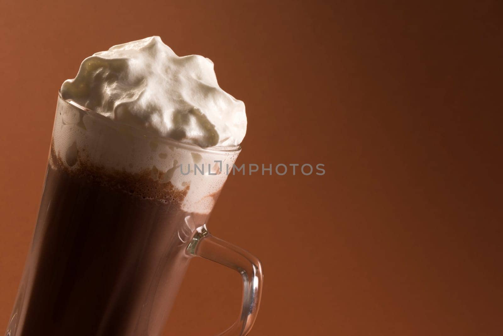 Hot chocolate drink or milkshake with whipped cream on brown background.