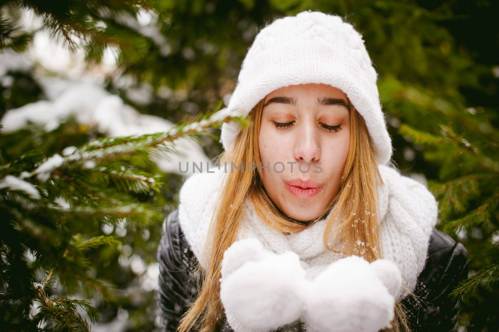 Blowing Snow. Beautiful Joyful Female Model on background of fir trees. Young woman enjoying magical snowfall. Winter wonderland.