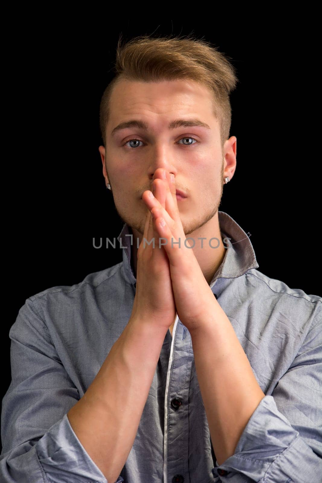 Attractive blond young man, serious expression with hands joined in front of mouth